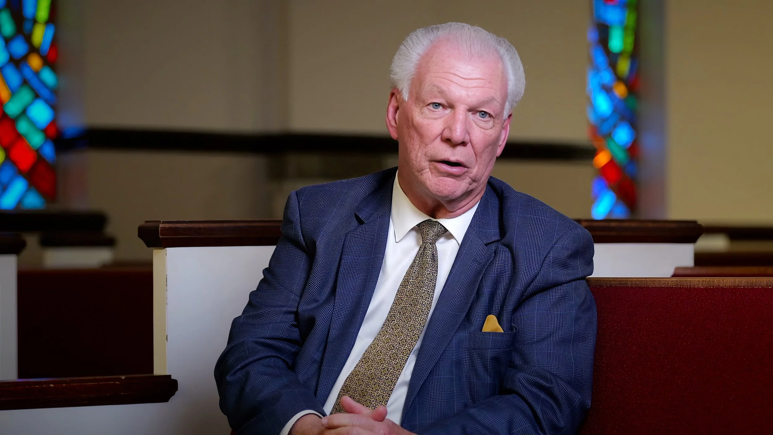 Professionally lit church documentary interview featuring Pastor Gilley, with balanced facial illumination and stained-glass windows in the background.