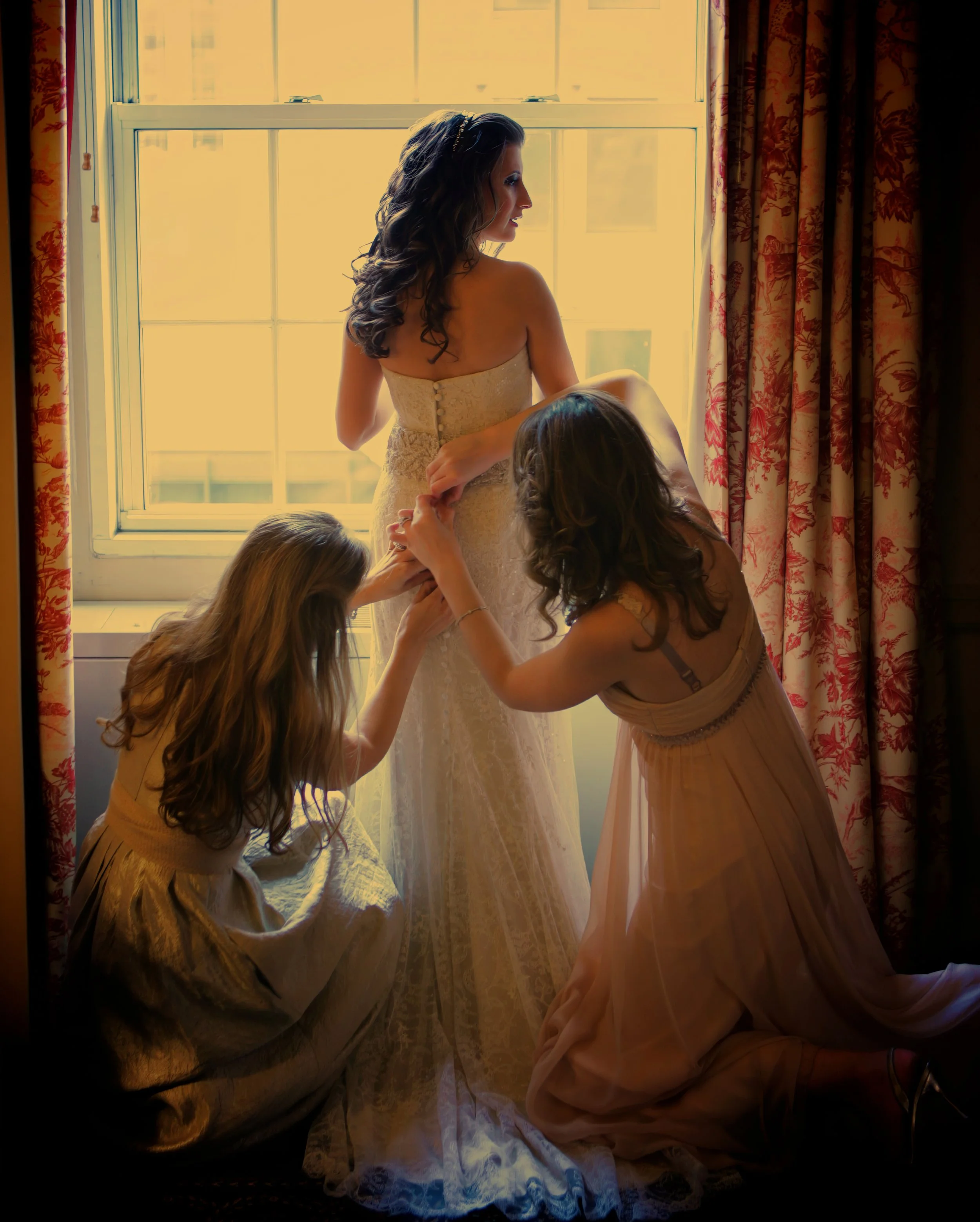 Bridesmaids assisting the bride with her dress in window light at the Yale Club