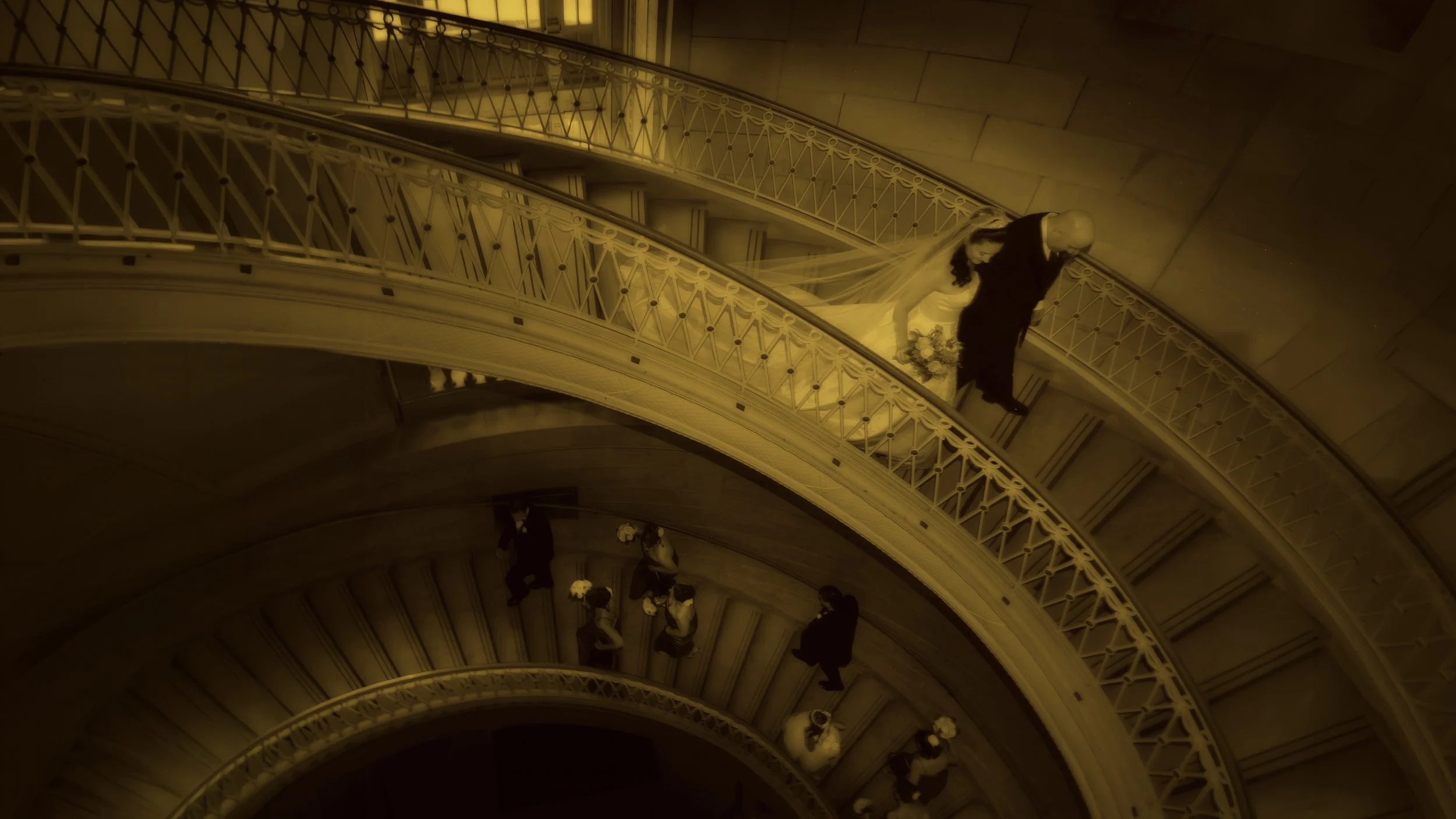 Bride and groom descend the winding staircase at Hartford City Hall with bridal party below, captured in fine art style.