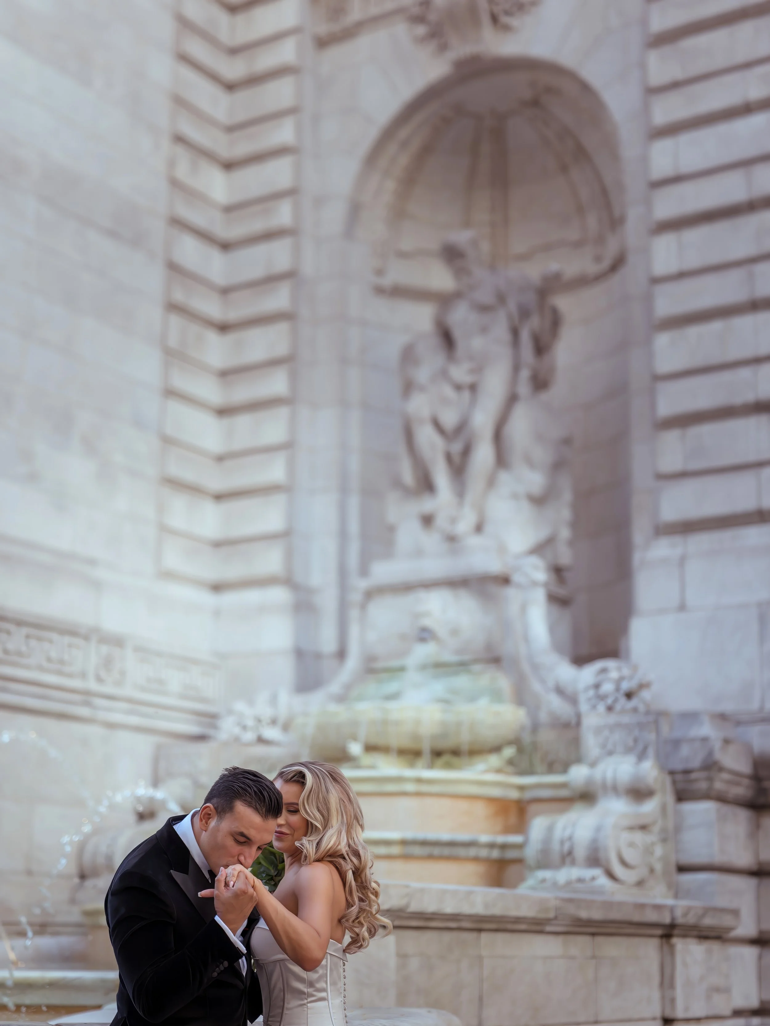 Groom kissing bride’s hand in a candid portrait by the fountain at the New York Public Library wedding