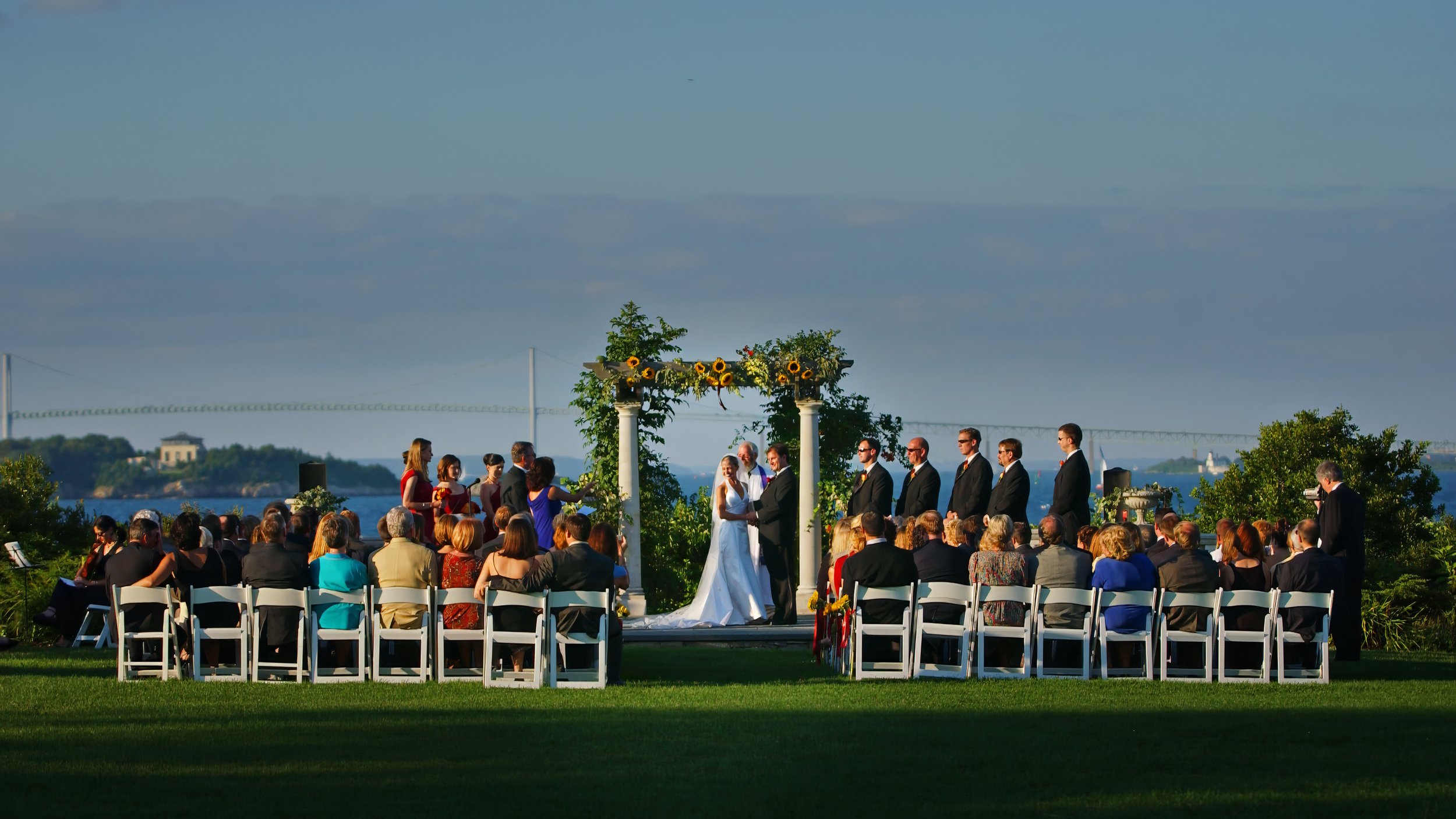 Sweeping view of an outdoor wedding ceremony at Castle Hill with Narragansett Bay in the background.