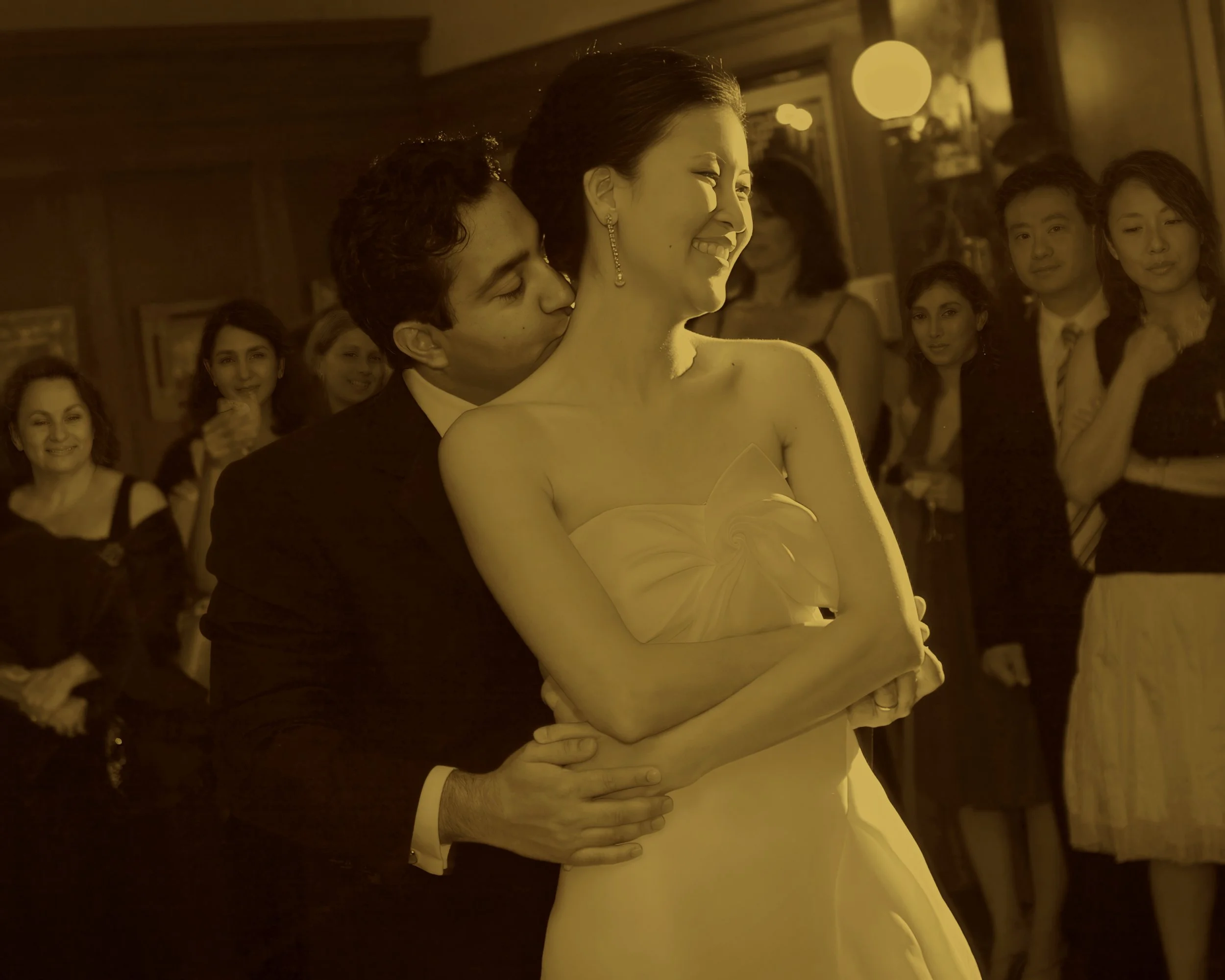 A groom kisses his bride on the neck during their first dance at the Union League Cafe in New Haven CT and her expression is timeless