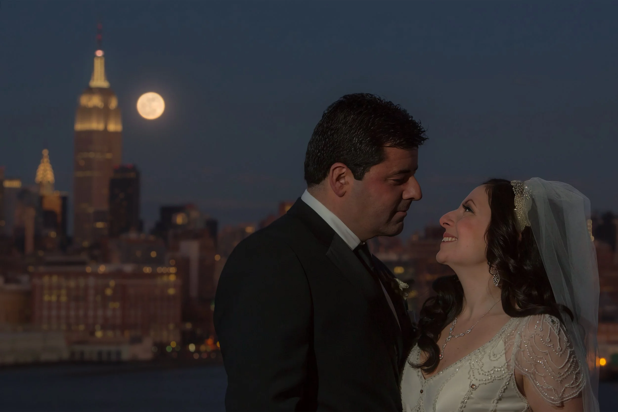 Bride and groom sharing a quiet moment beneath the Manhattan skyline and a glowing full moon near W Hoboken.