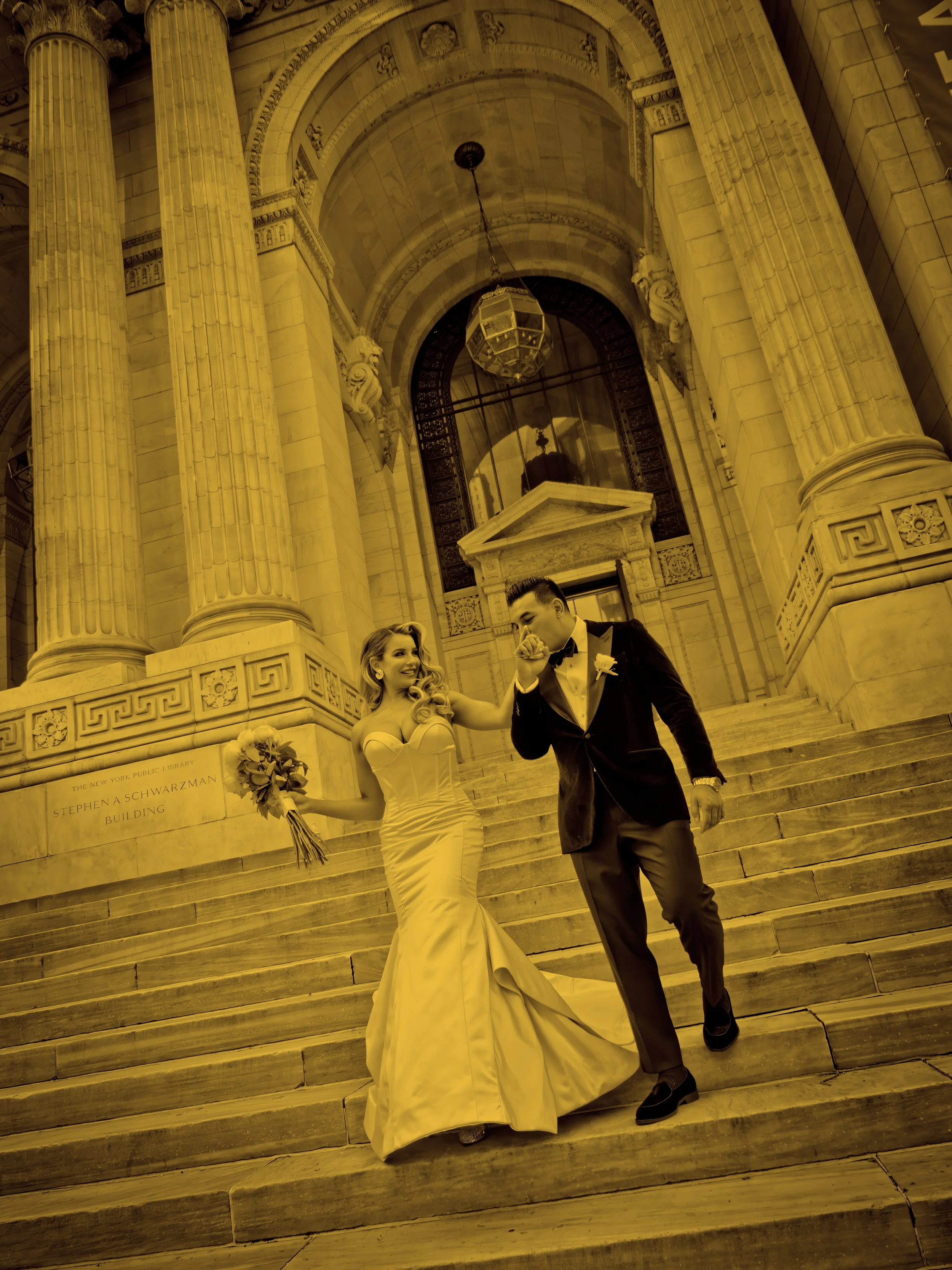 Groom kisses the bride’s hand as the couple descends the grand steps of the New York Public Library in Midtown Manhattan.