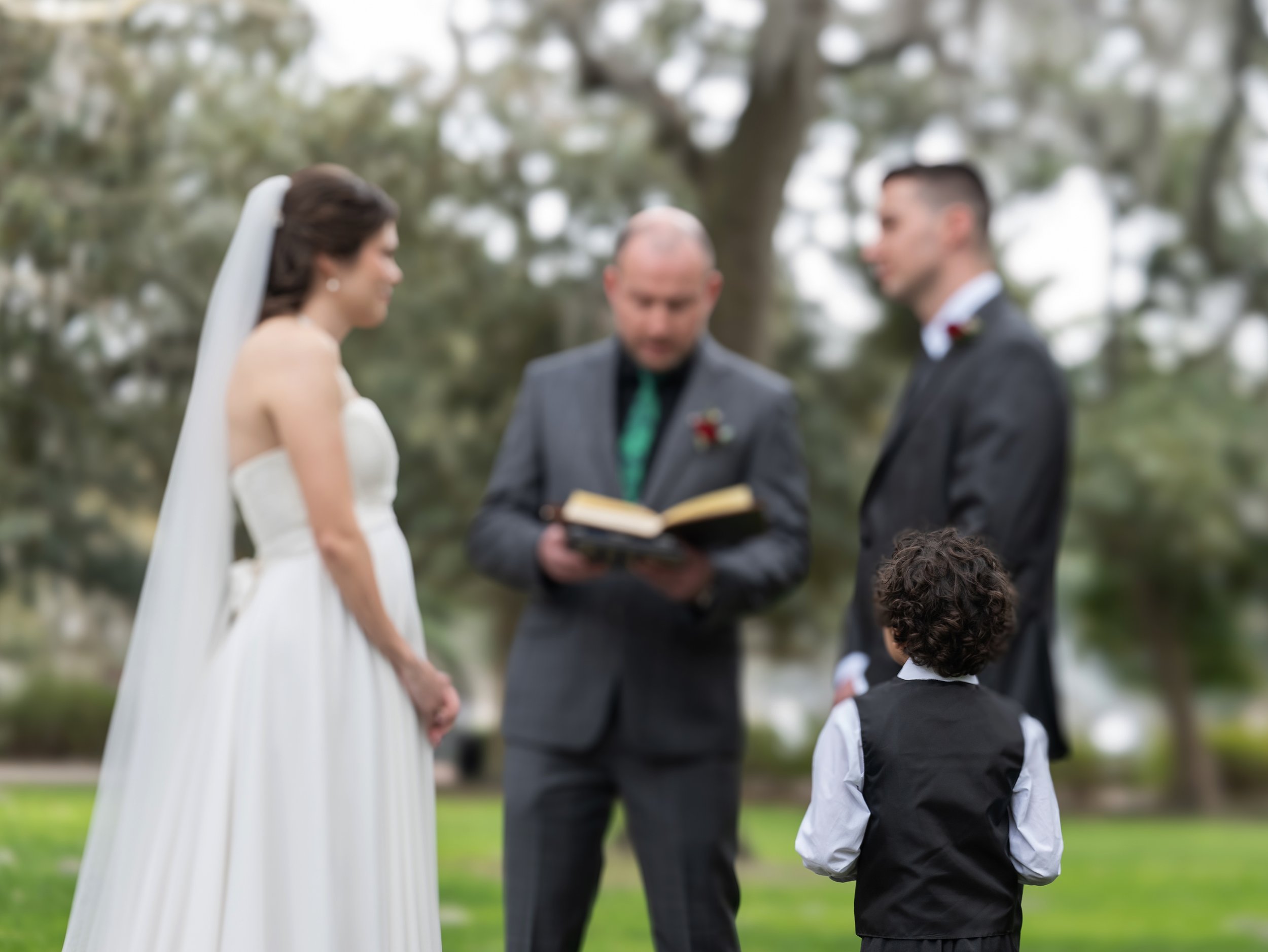 Tim and Daniella exchange wedding rings as their child looks up at them during their intimate Forsyth Park ceremony.