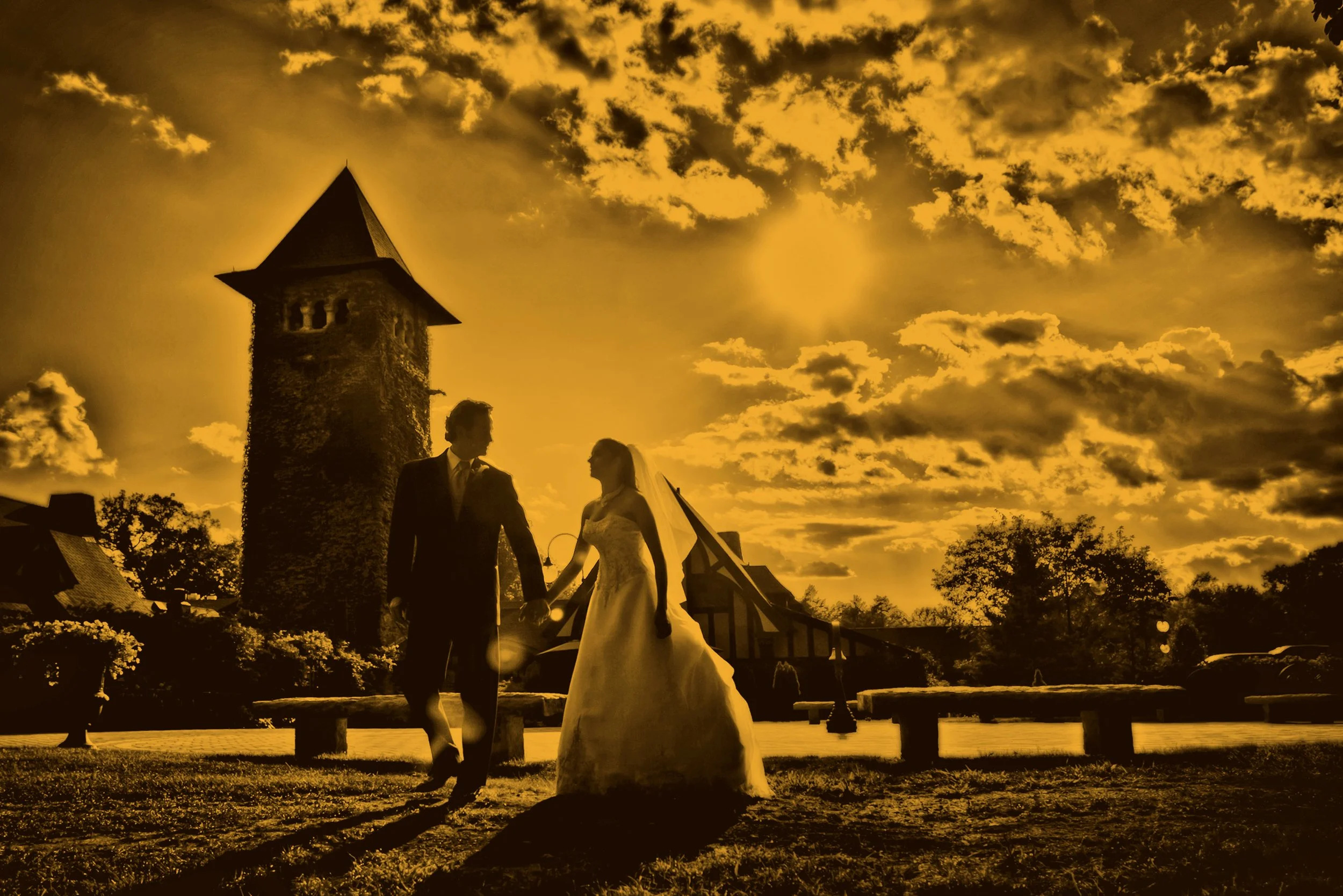 Fine art silhouette of bride and groom walking hand in hand beneath dramatic skies and the Saint Clements Castle tower.