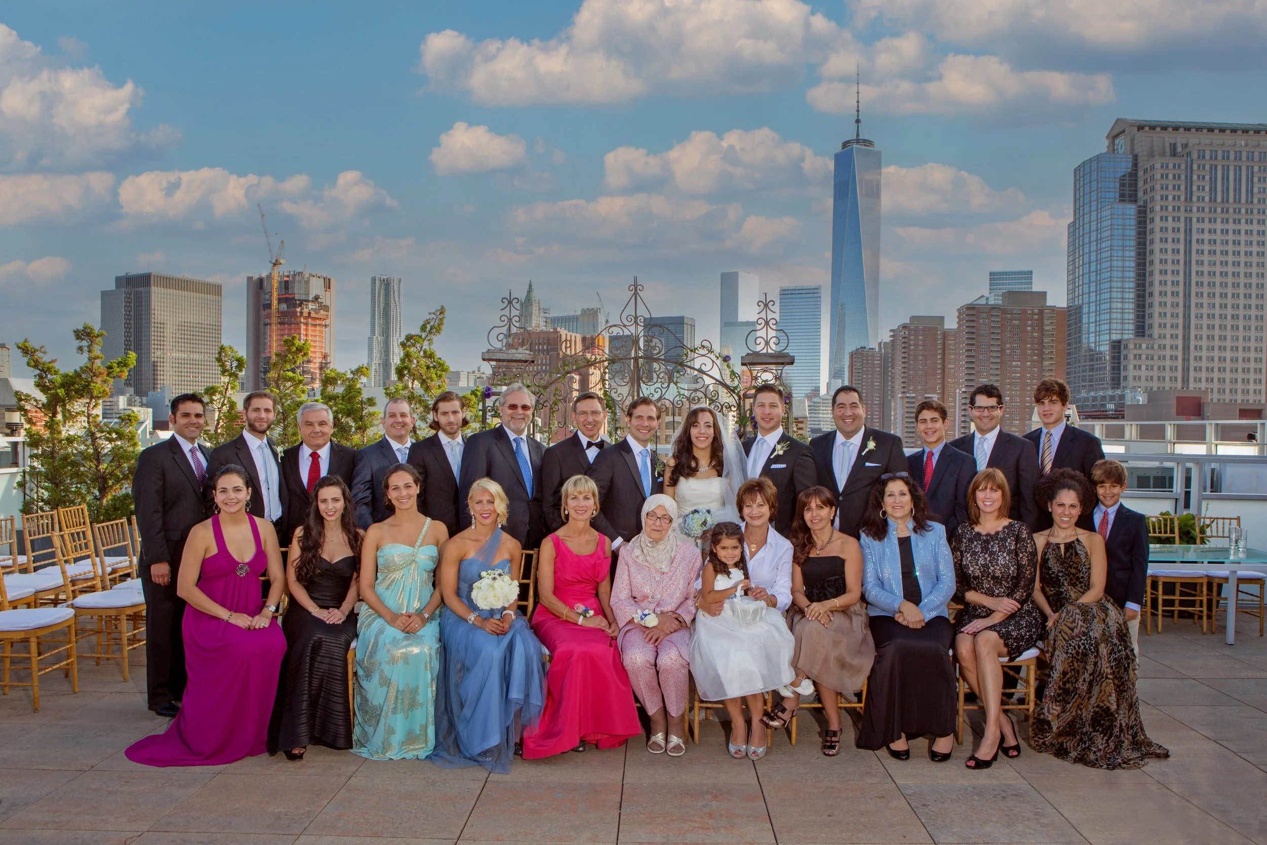 Large family portrait photographed on the rooftop terrace with sweeping Manhattan skyline views behind the group.