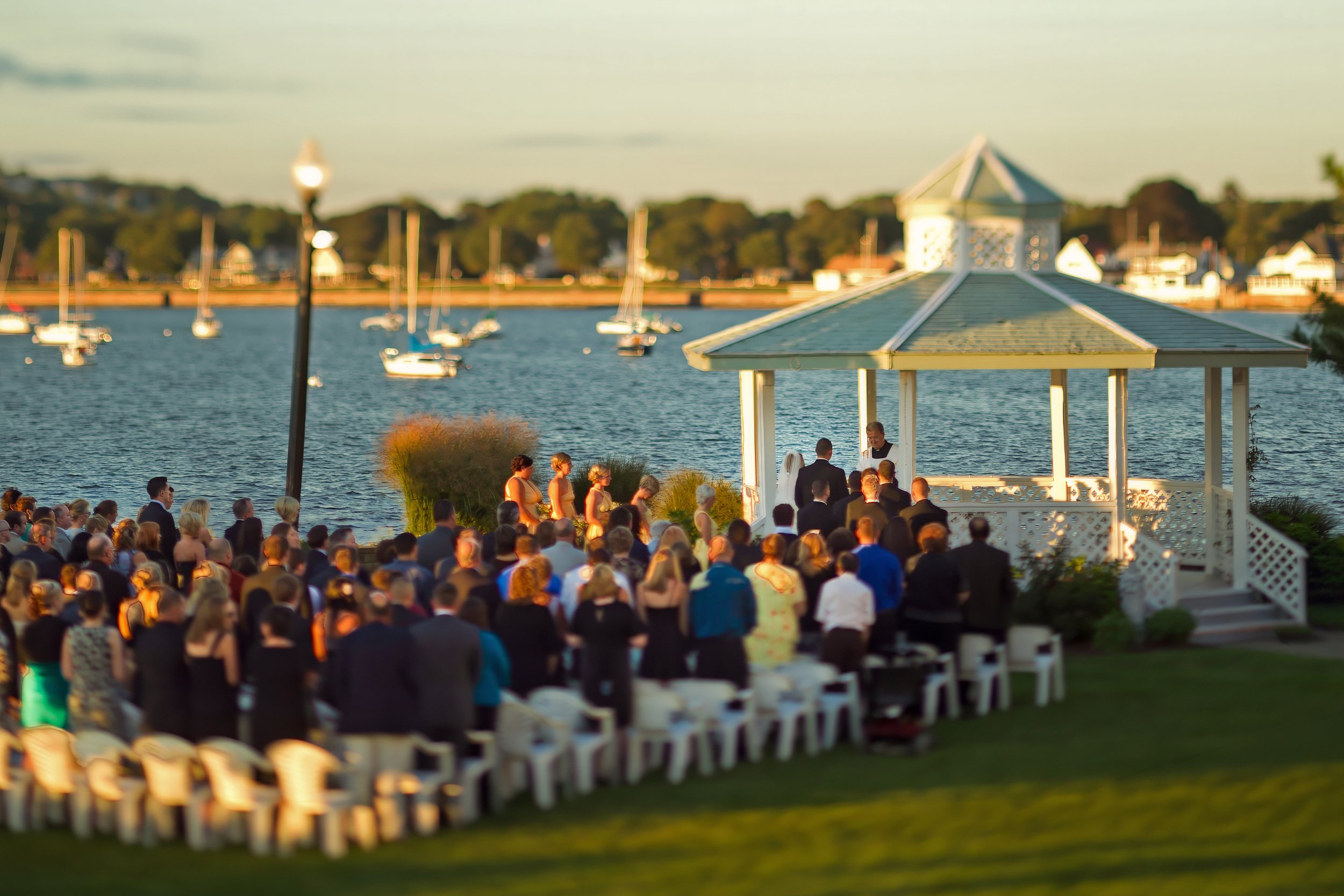 Wide view of wedding ceremony on the lawn at Amarante’s Sea Cliff with sailboats in New Haven Harbor