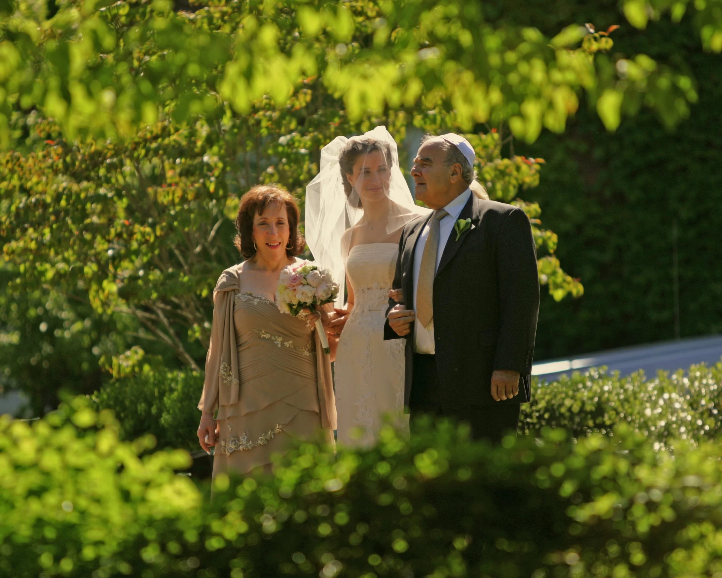 Bride shares a quiet moment with her parents before walking down the aisle at an outdoor ceremony.