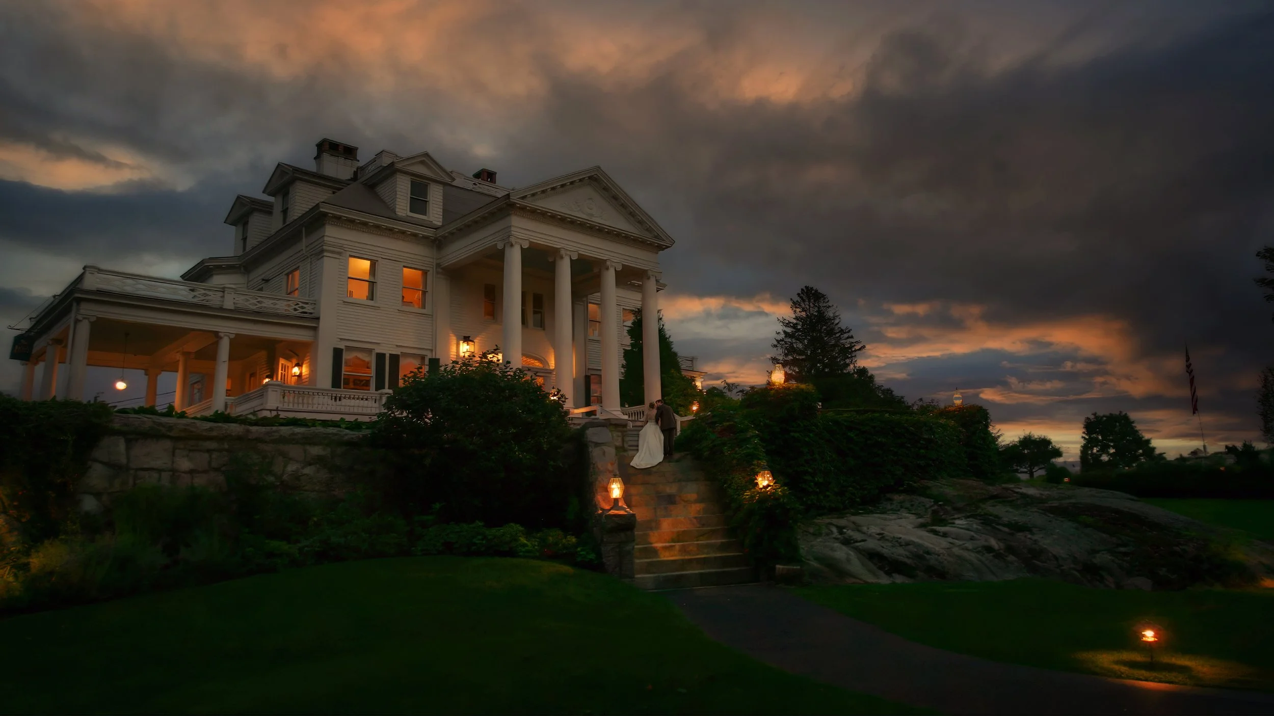 A bride and groom kiss on the steps in front of the Inn at Mystic