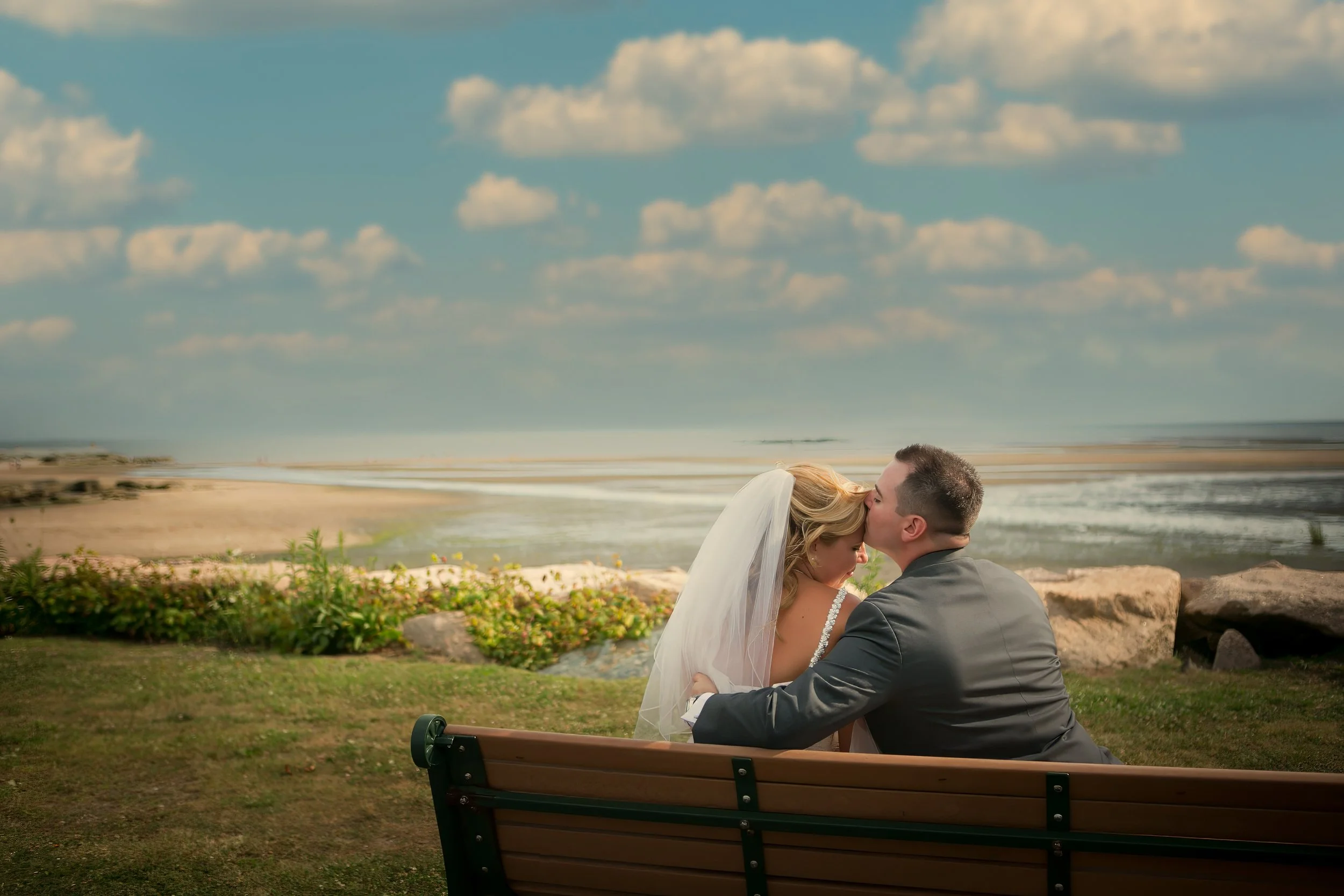 Bride and groom sharing a romantic moment on a park bench overlooking Long Island Sound at Lighthouse Point Park in New Haven Connecticut