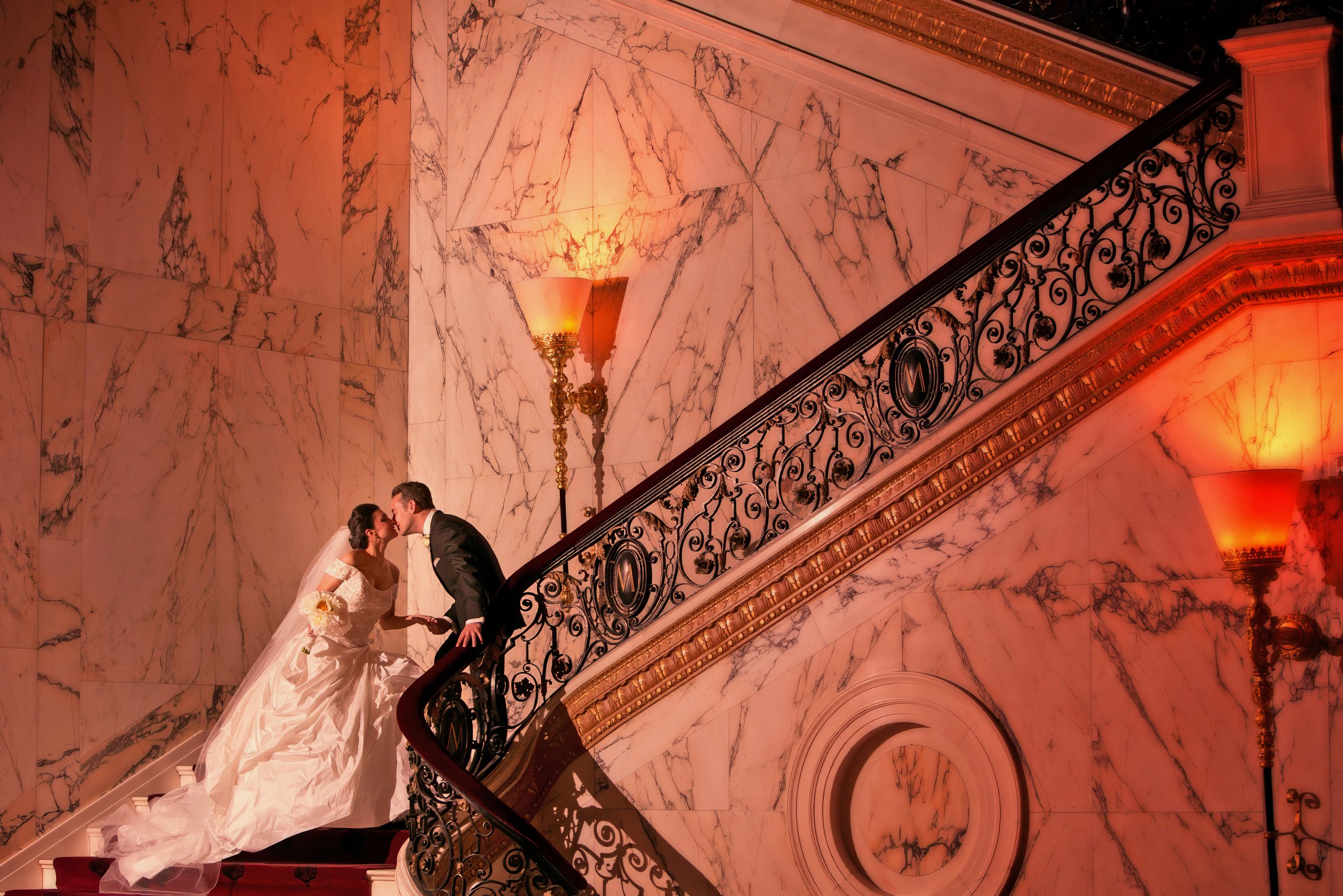 Bride and groom sharing a legacy portrait kiss on the grand staircase during a wedding reception at the Metropolitan Club in New York City.