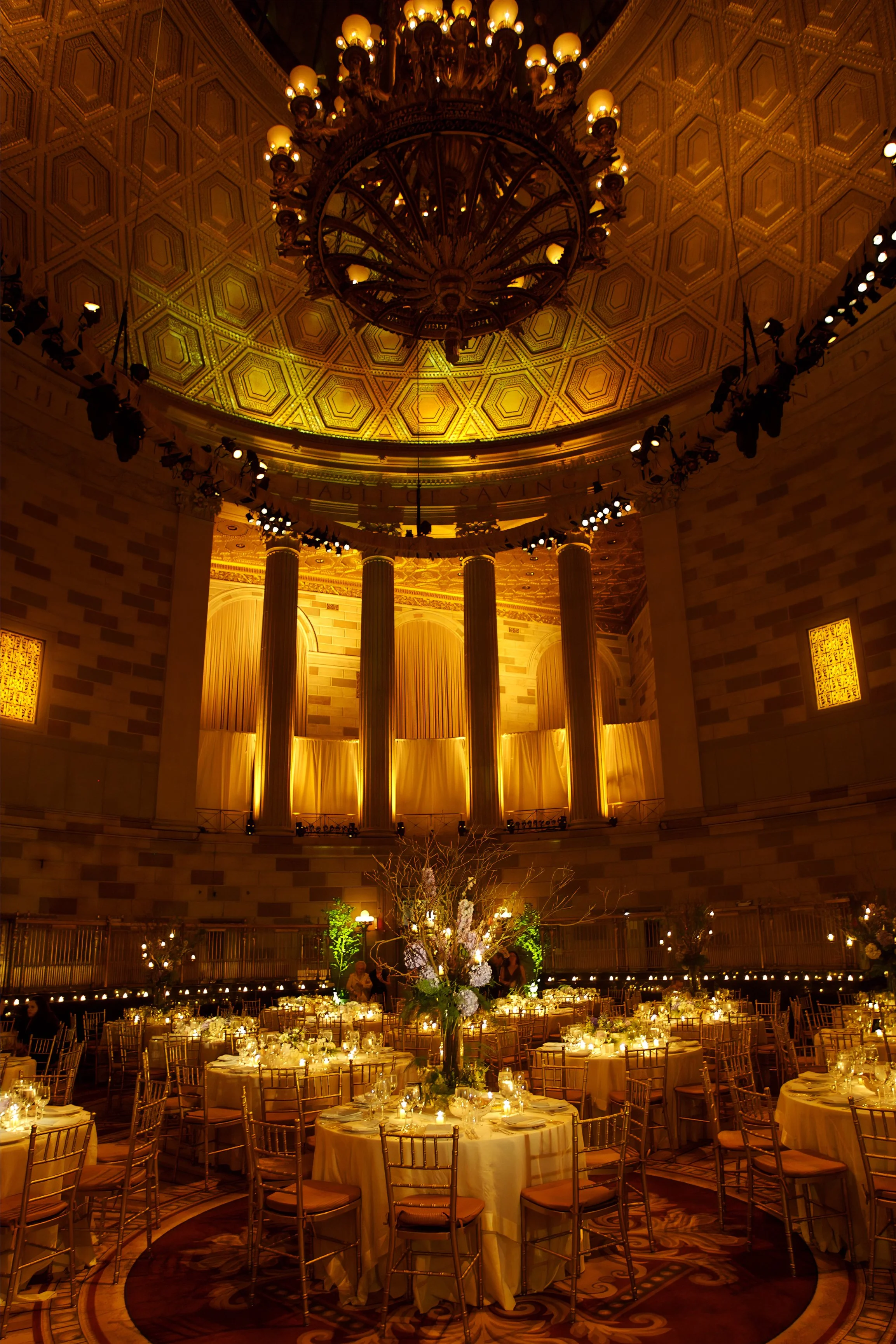 Elegant wedding reception table settings beneath the 70-foot dome of Gotham Hall with amber lighting and candlelight.