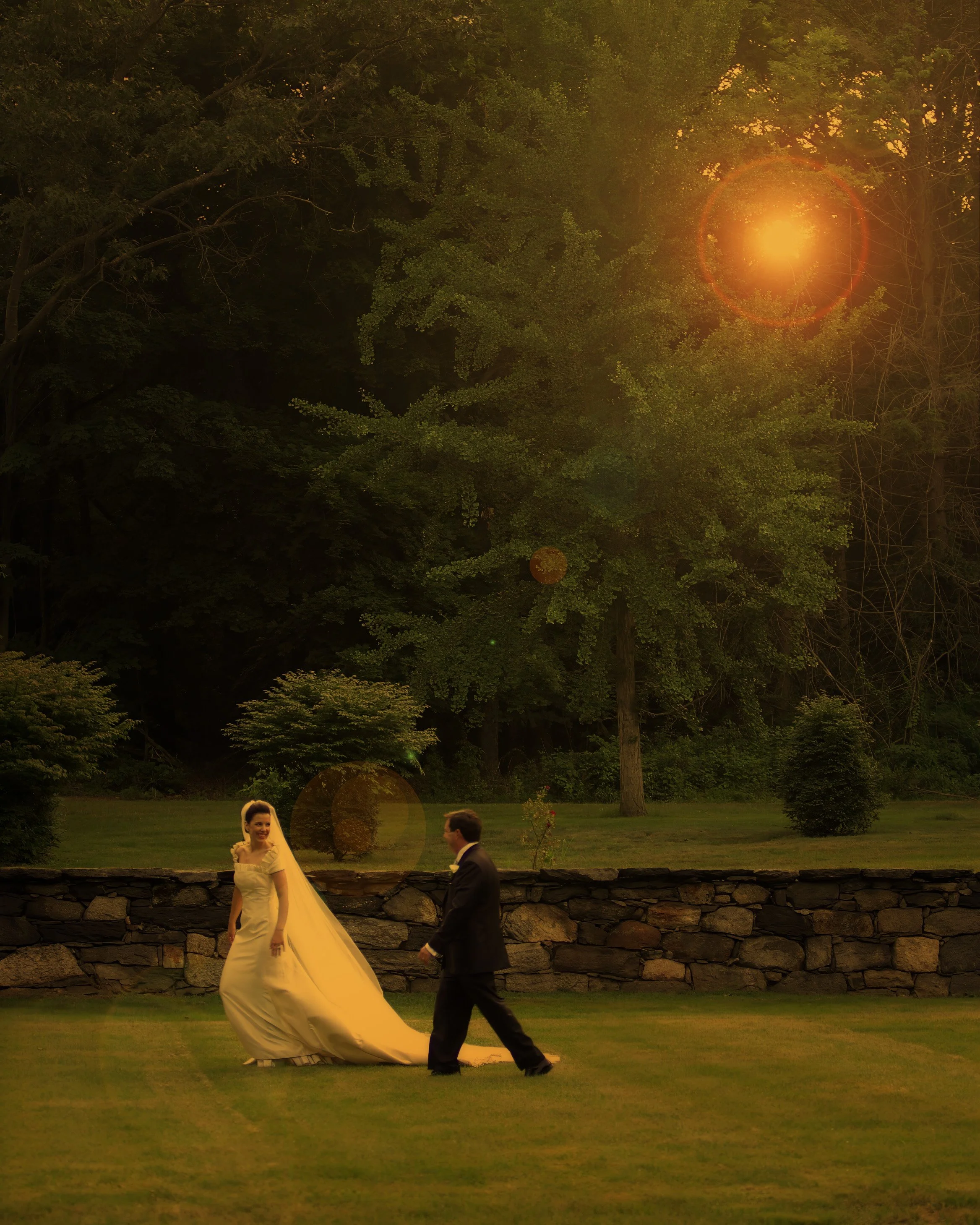 Bride and groom walking playfully through the Sunken Gardens at Saint Clements Castle with sunlight filtering through the trees