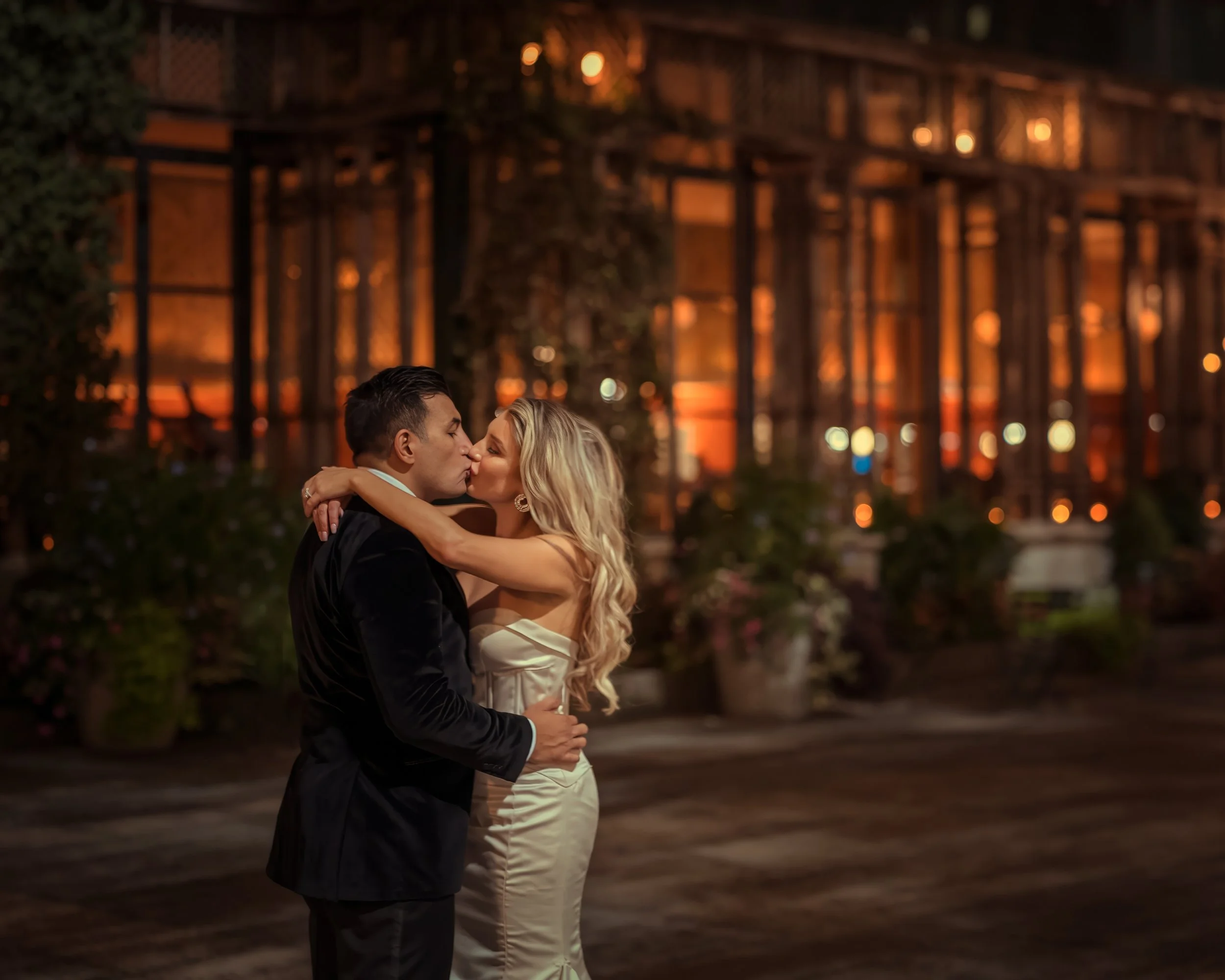 Bride and groom kiss at night with Bryant Park Grill illuminated in Midtown Manhattan