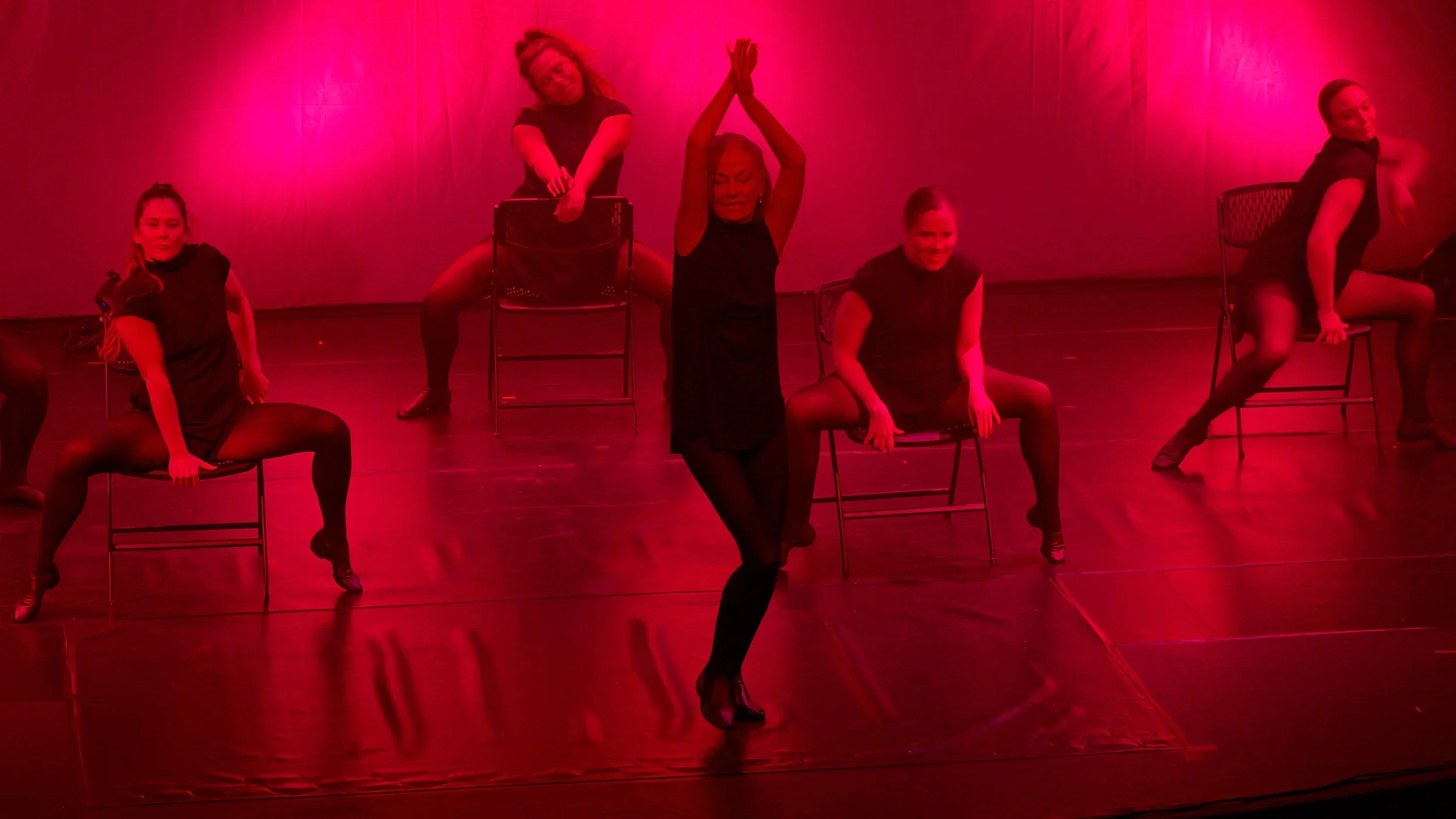 Contemporary dancers perform choreography with chairs beneath dramatic red theatrical lighting during Tybee Ballet Theatre's From the Minds of Others.