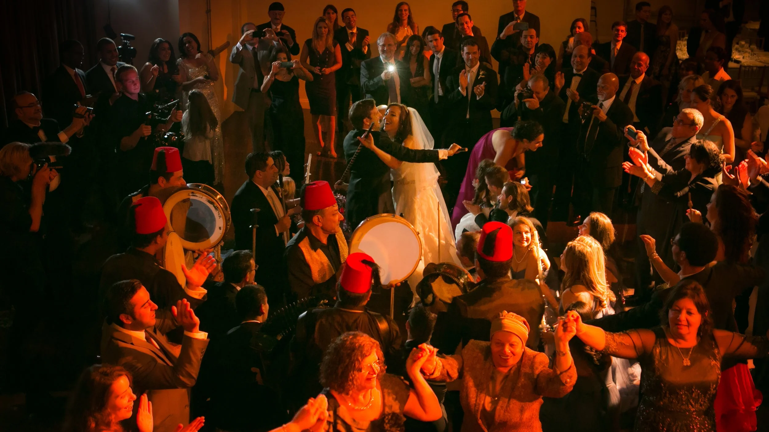 Bride and groom celebrating at the center of a lively cultural dance during their wedding reception.