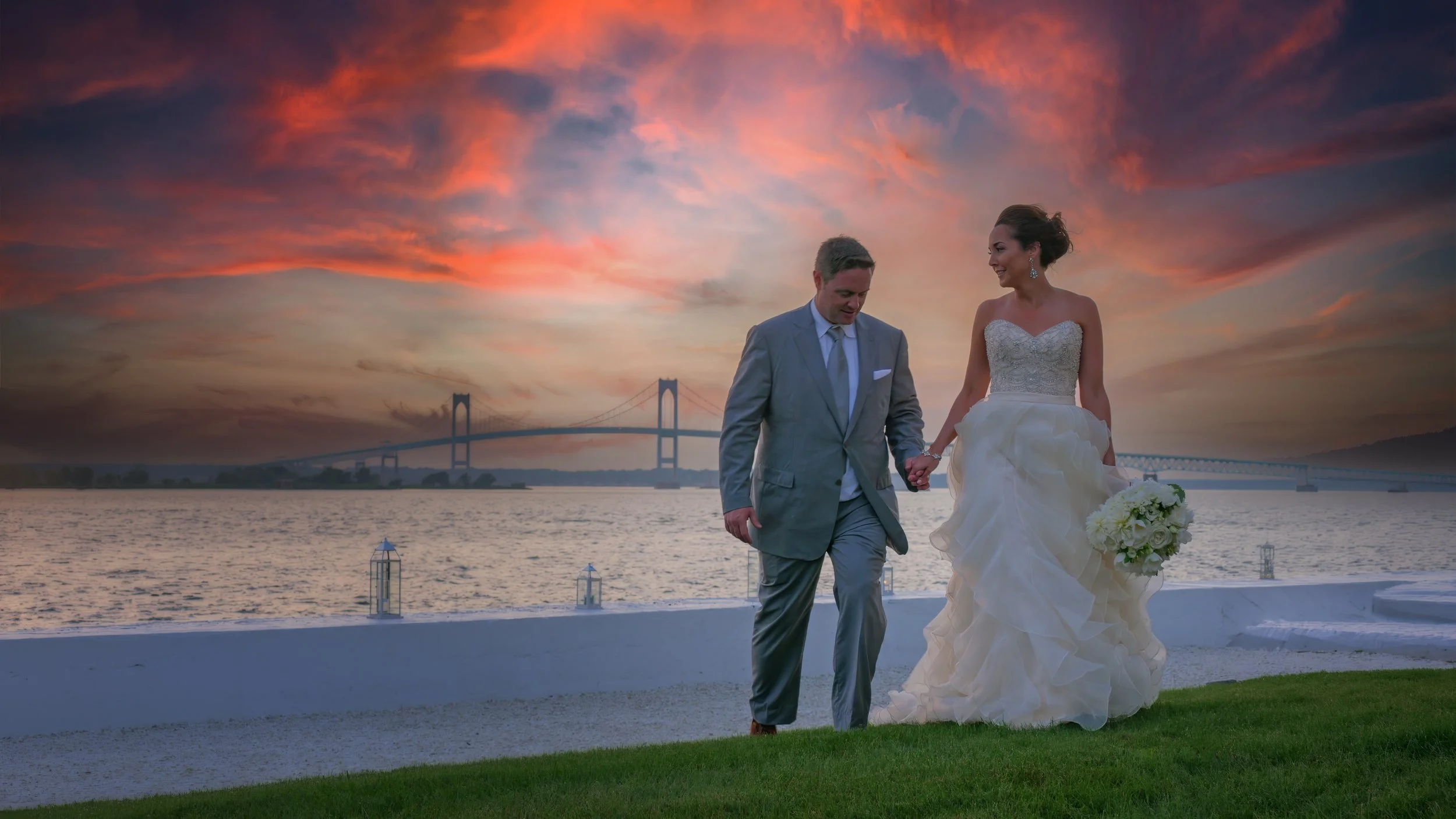 Bride and groom walking the grounds of Belle Mer in Newport Rhode Island during sunset with the Newport Bridge in the distance.