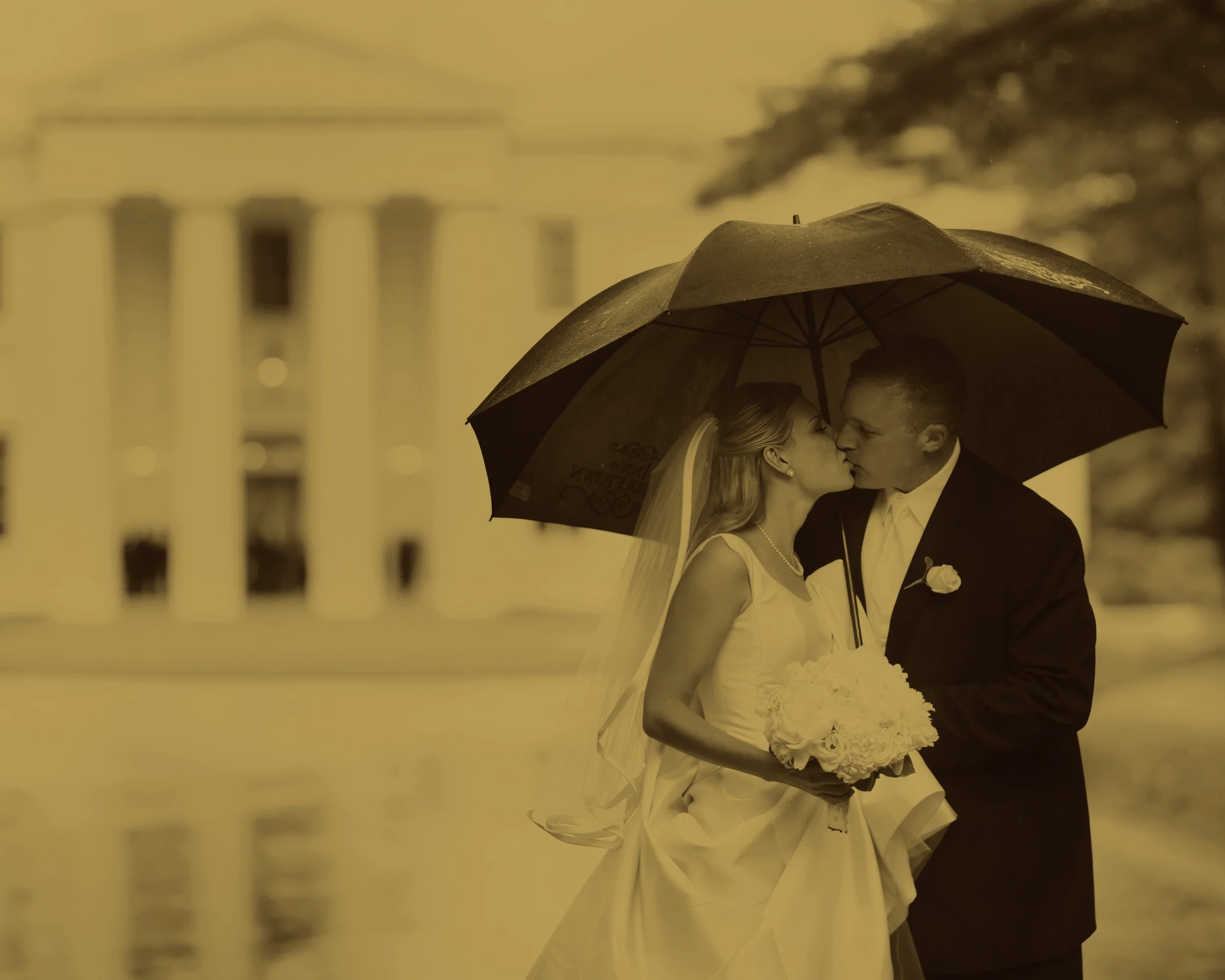 Bride and groom kissing under an umbrella in the rain with a Connecticut mansion in the background.