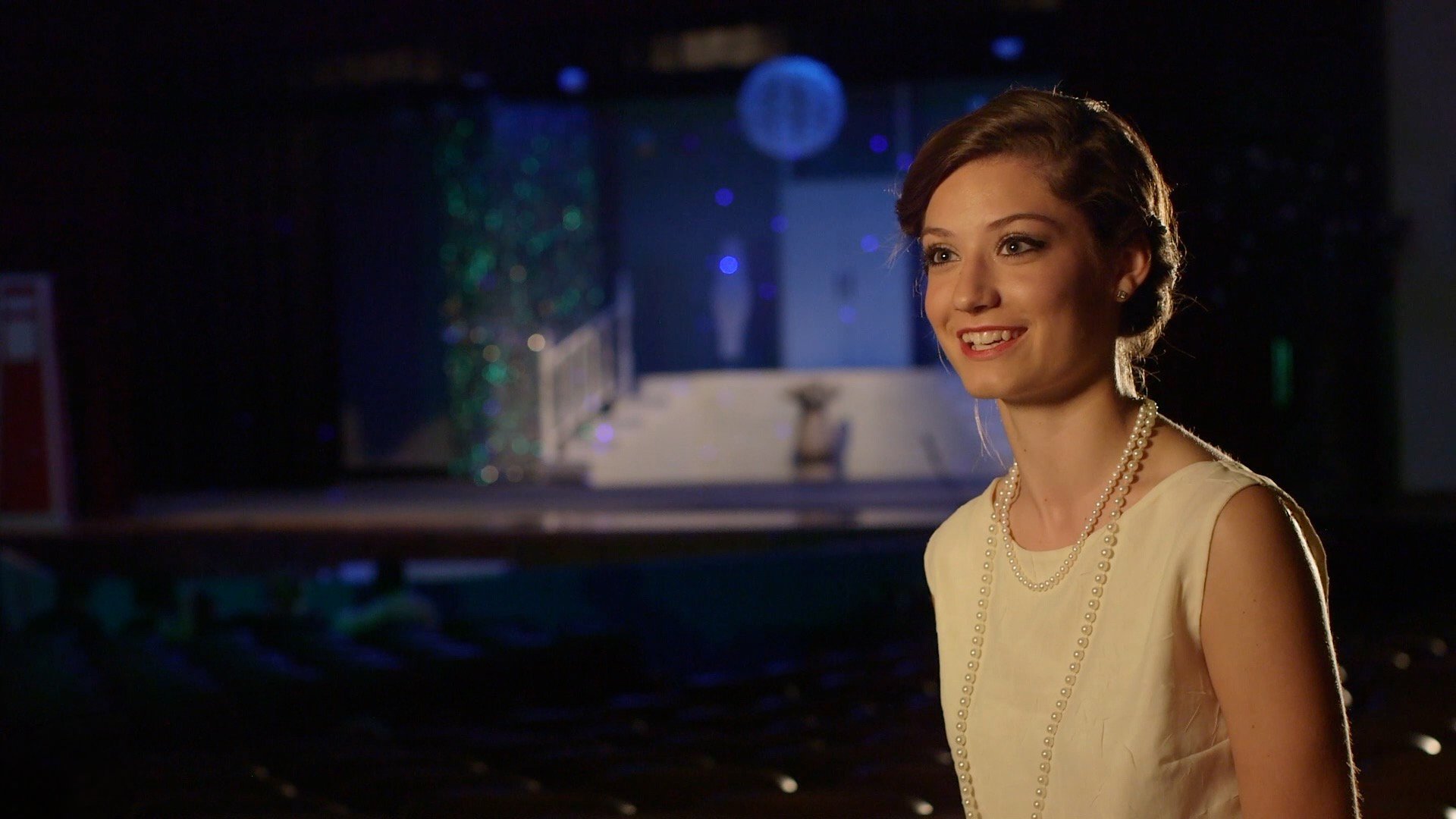 Actress wearing a cream period dress and pearls during a professionally lit interview for Sheehan High School's production of The Great Gatsby.