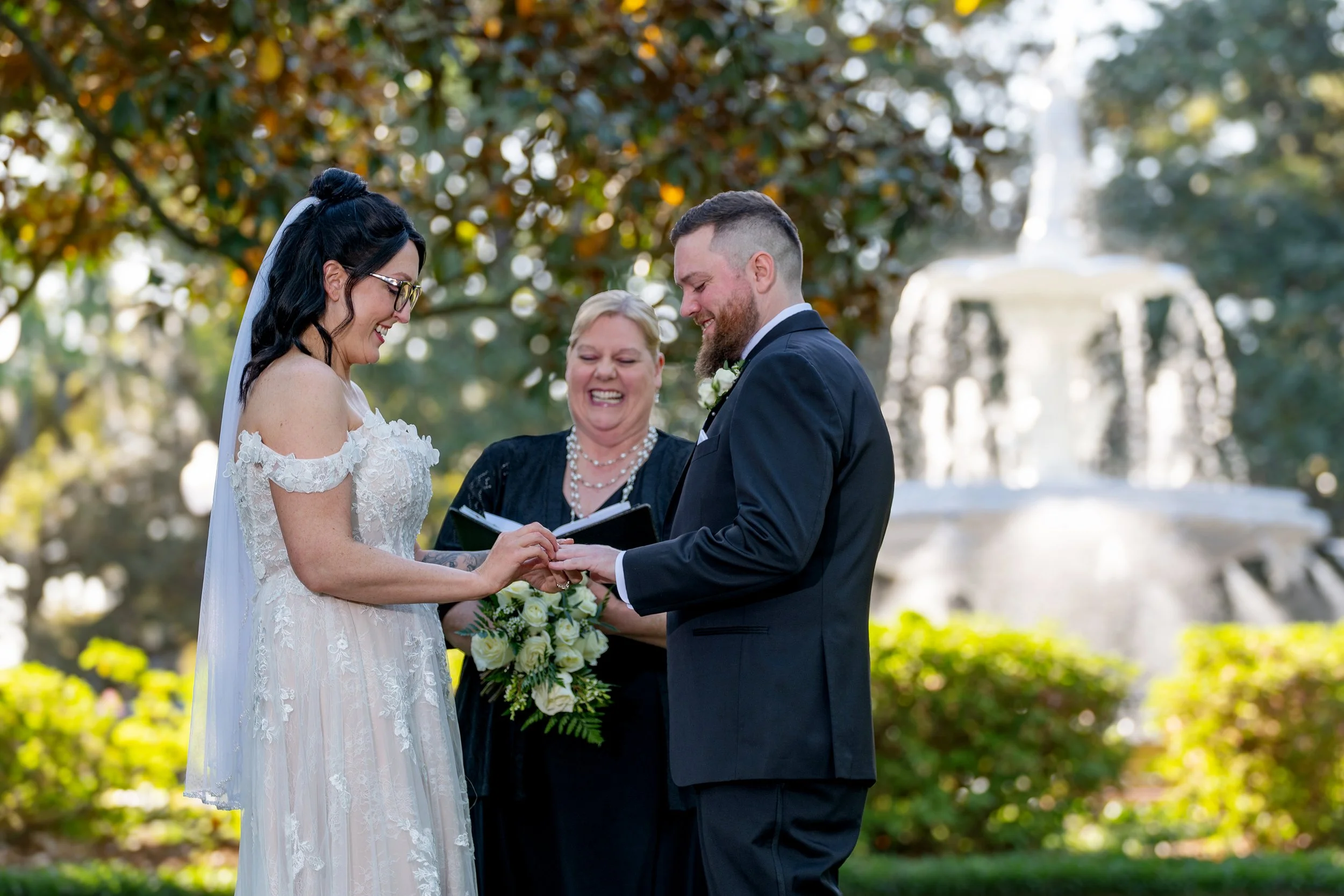 Bride and groom exchange rings beside the Forsyth Park fountain in afternoon sunlight during a Savannah elopement.