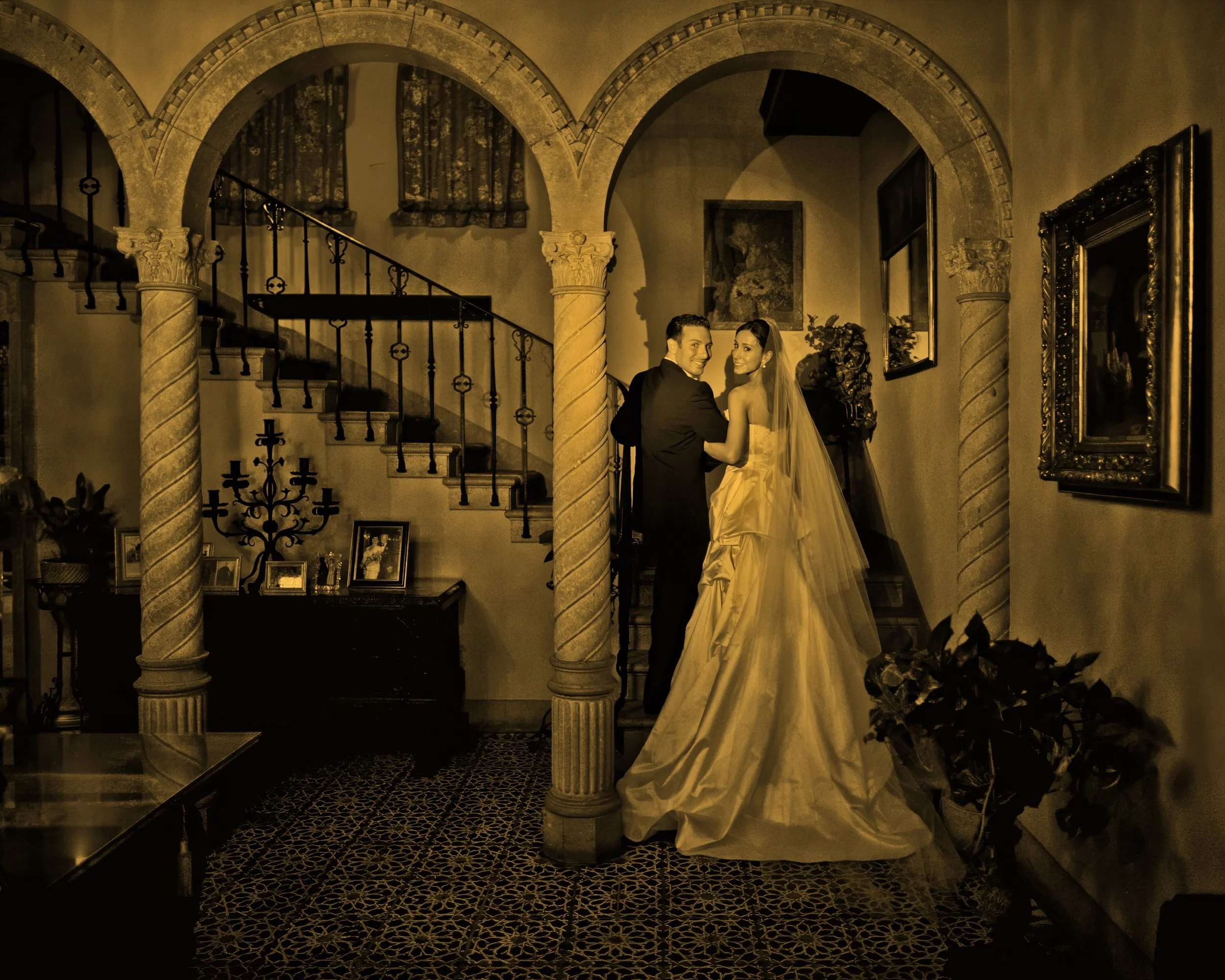 Bride and groom glance back toward the camera while standing on the grand staircase beneath the archways inside Pleasantdale Chateau.
