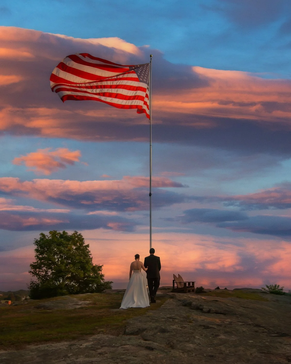 Bride and groom walk arm in arm to the bluff at sunset with an American Flag waving in the wind at the Inn at Mystic.