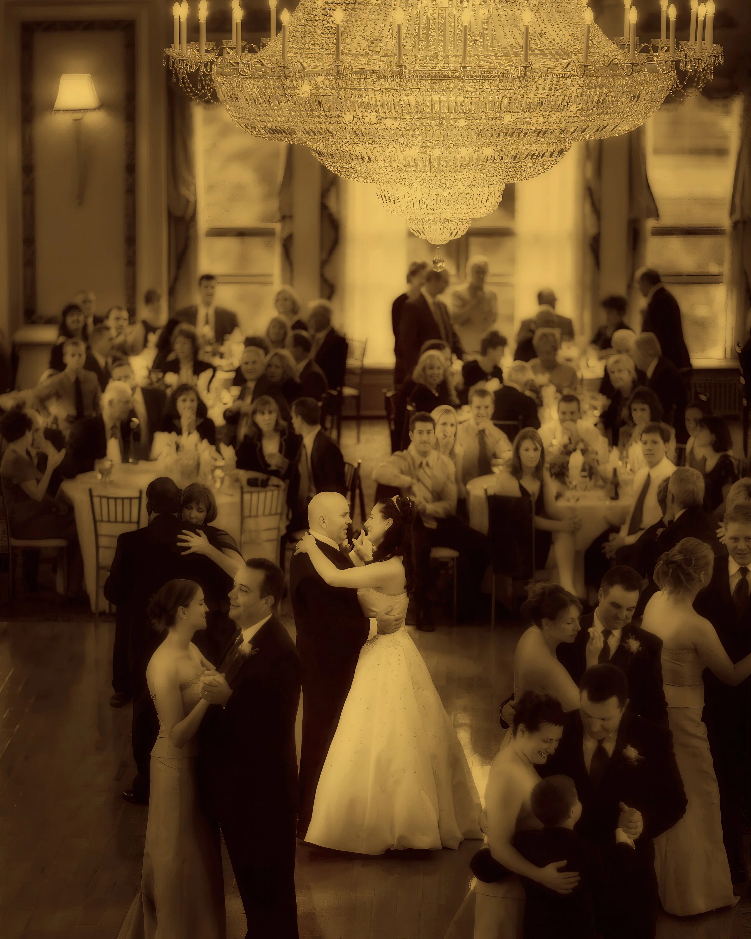 Bride and groom dance beneath the grand chandelier alongside their bridal party as guests look on in Bond Ballroom.