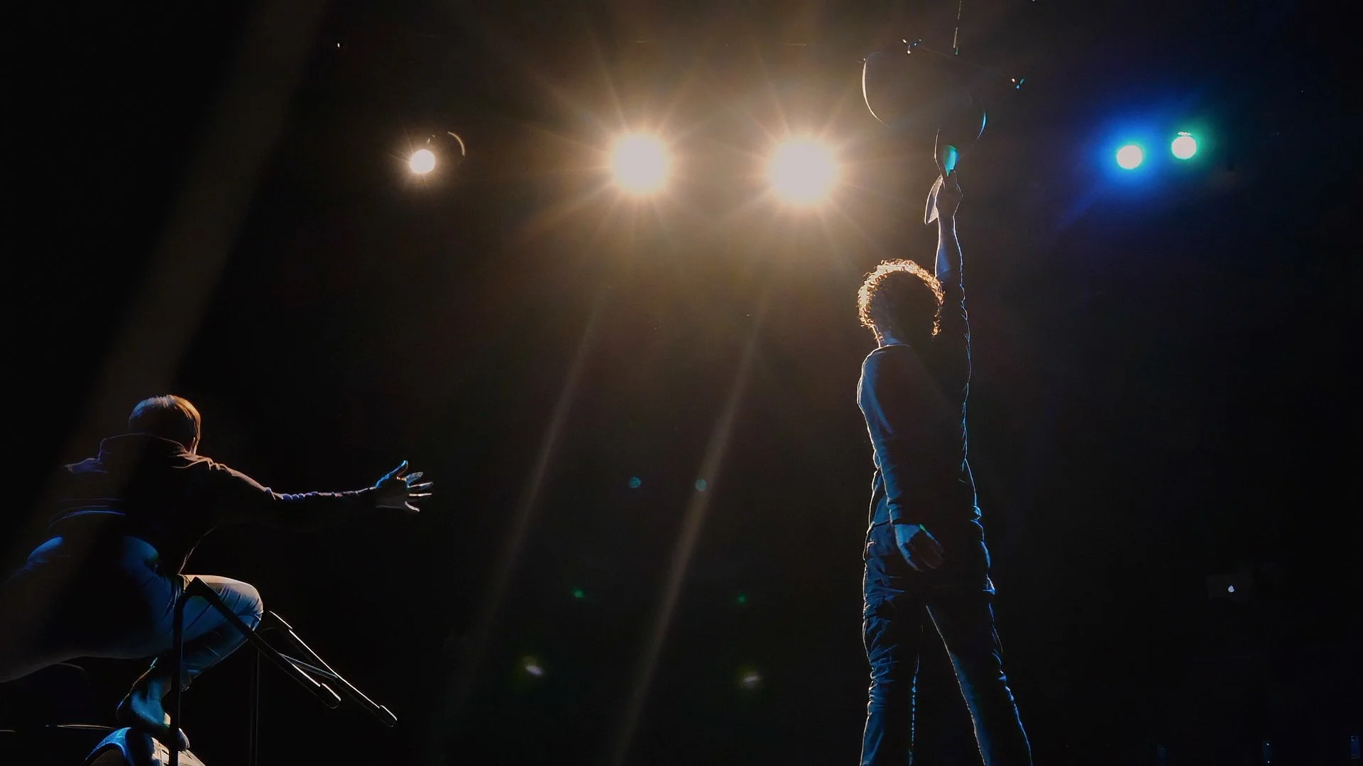 Performers use chairs and expressive physical movement on a minimalist black stage during the Masks and The Monster theatrical workshop.
