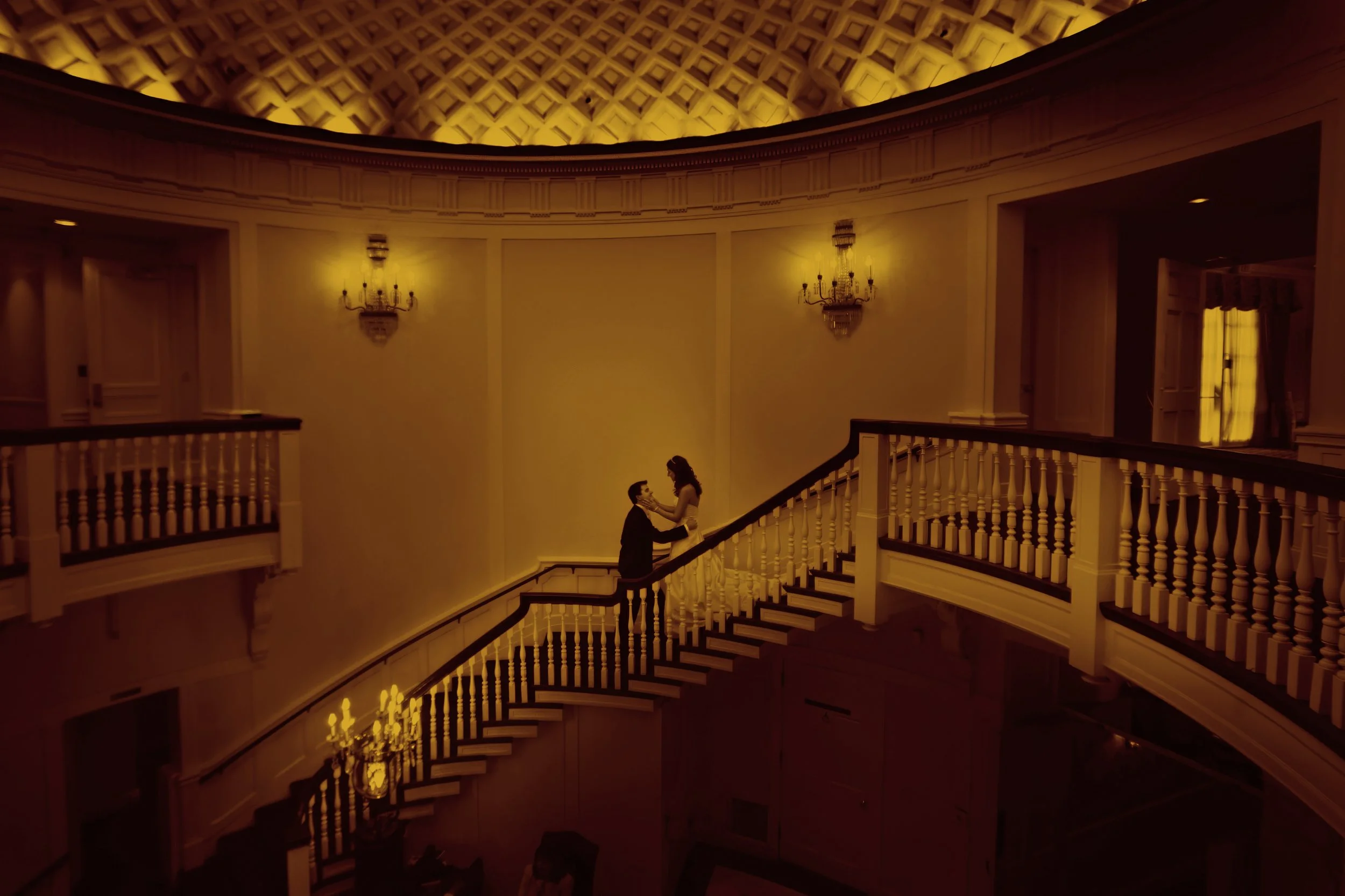 Bride and groom embrace during their first look on a grand staircase beneath an illuminated domed ceiling.