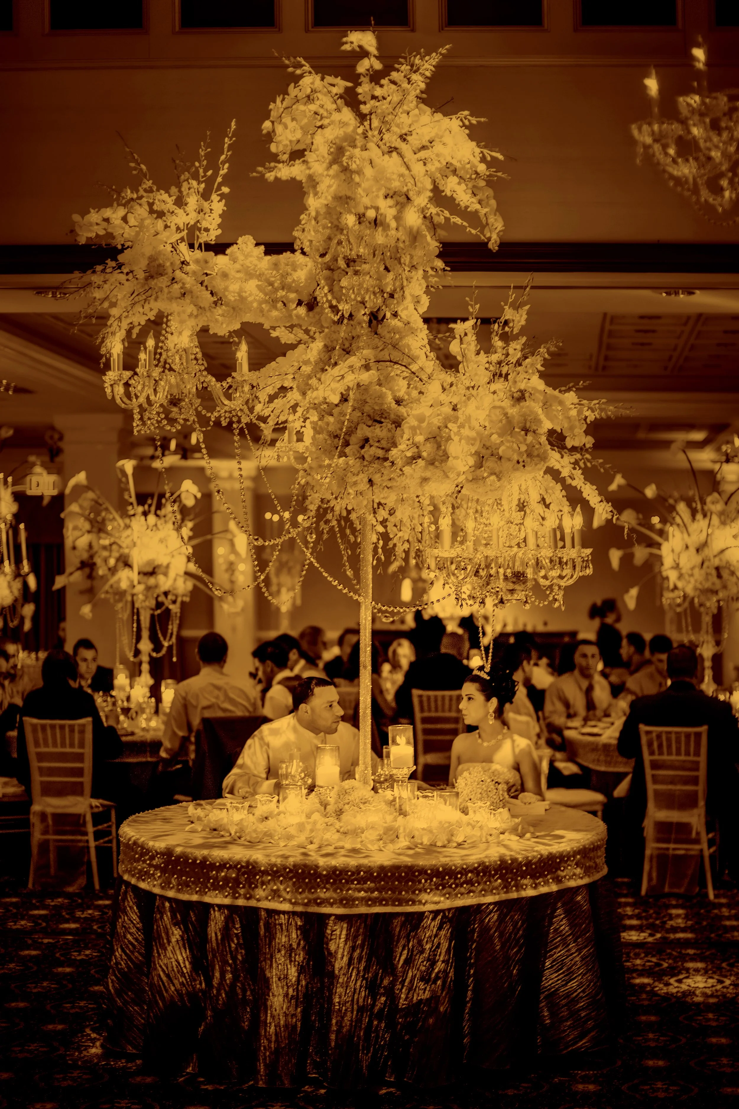 Bride and groom sit at their sweetheart table under opulent floral arrangements by David Tutera.