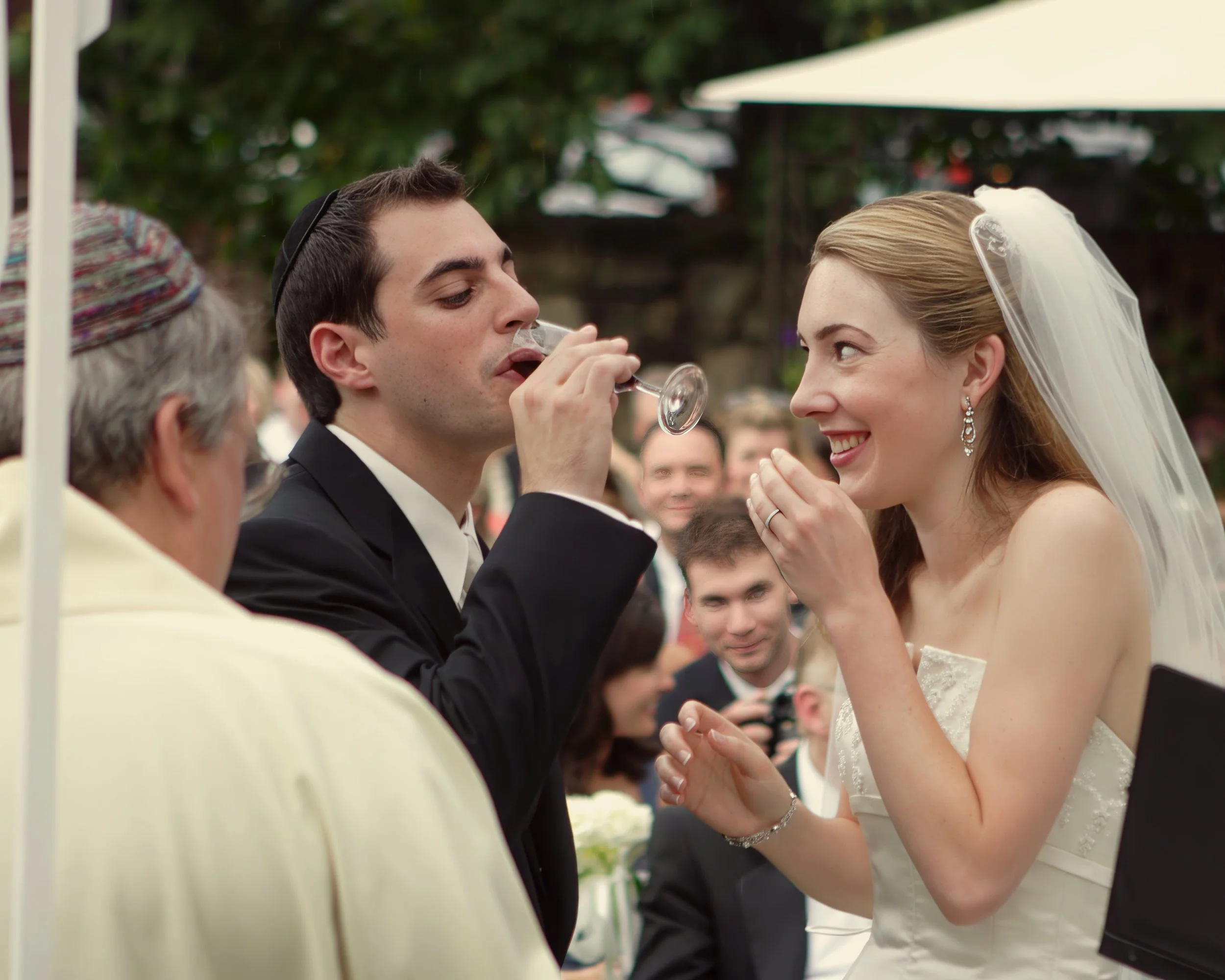Bride laughs as groom takes a sip of wine during the wedding ceremony at Le Chateau