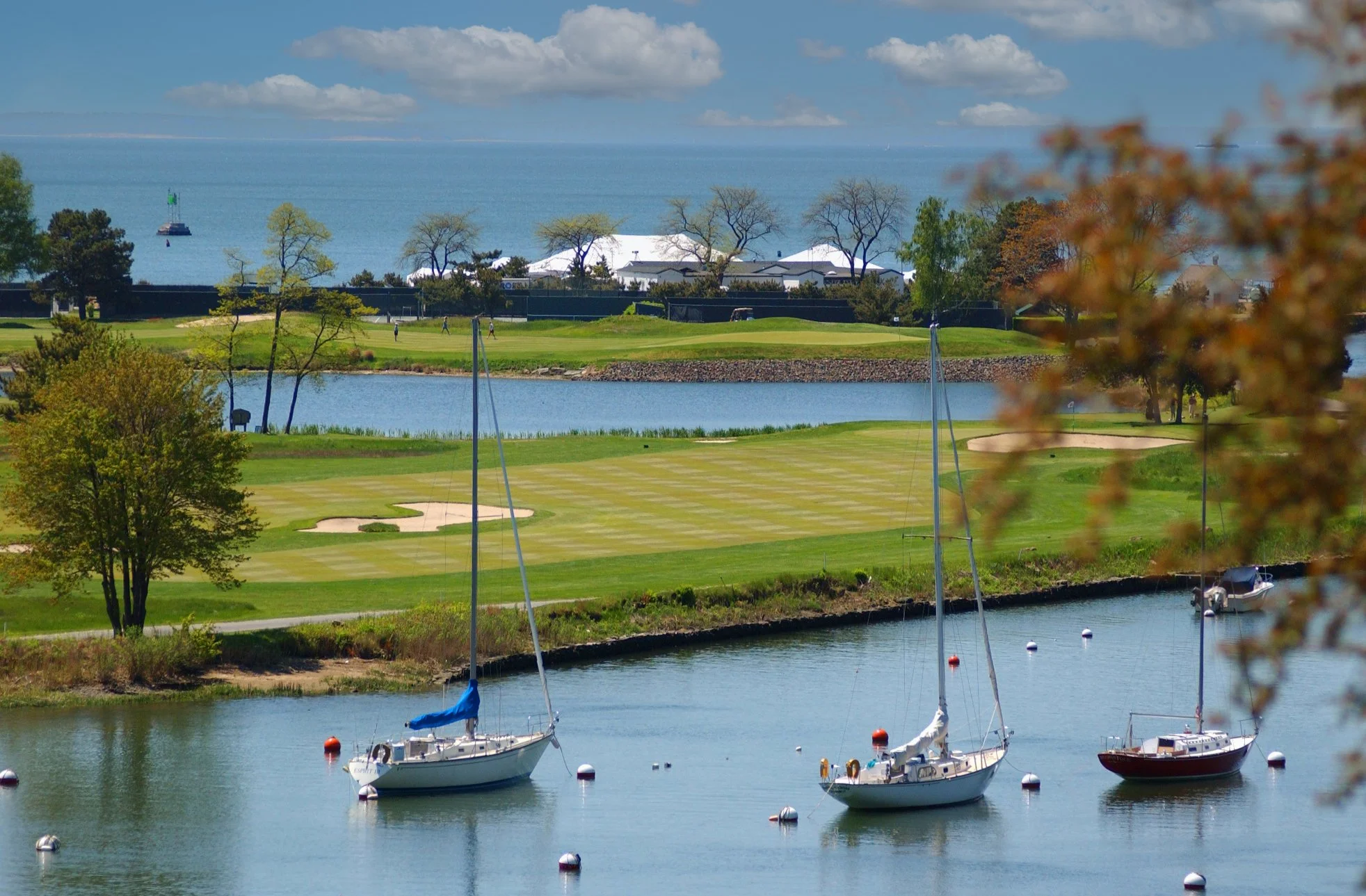 Sailboats moored in the harbor overlooking a tented wedding celebration on the shoreline in Southport, Connecticut.