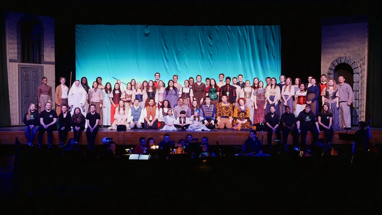 Large cast of student performers gathered on stage during Maloney High School's production of Les Misérables, with the orchestra pit visible.