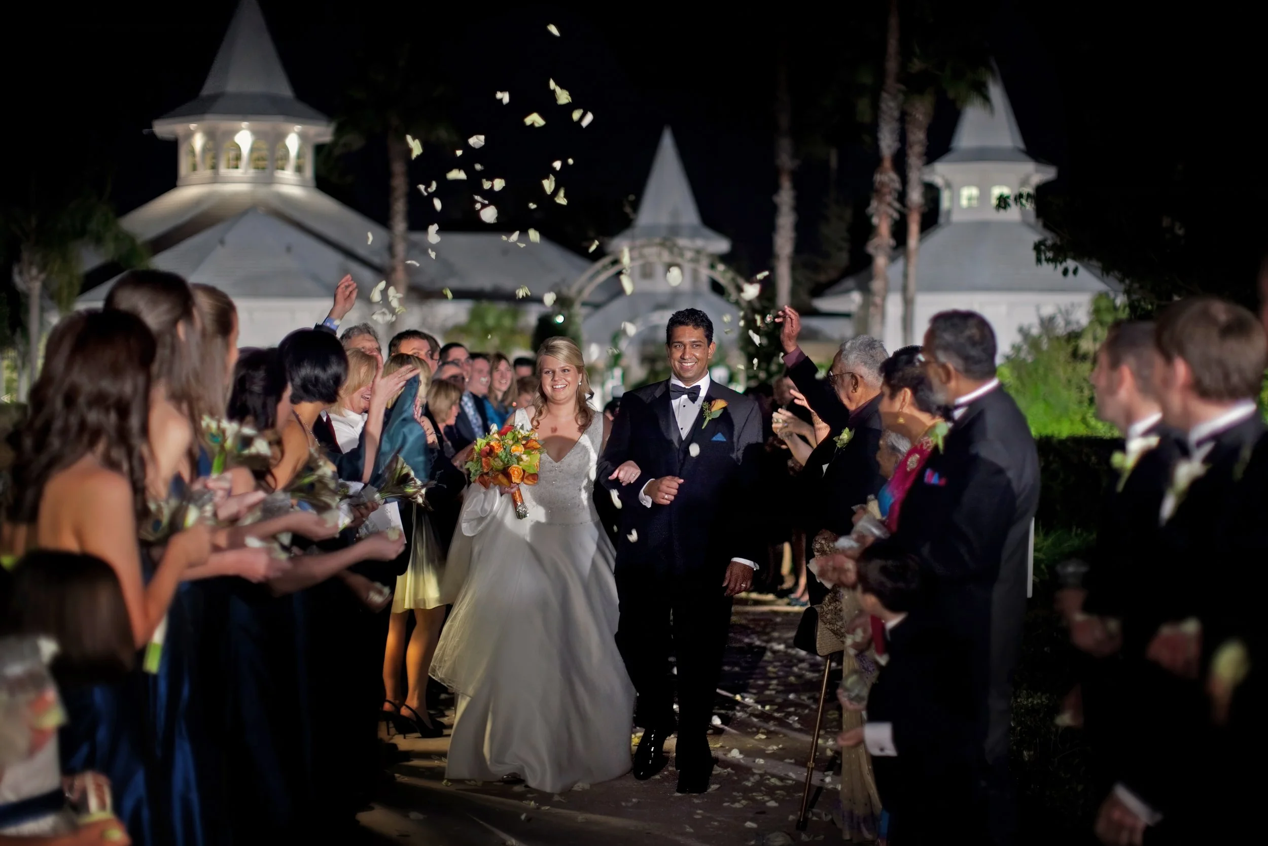Bride and groom exit the Disney Wedding Pavilion as rose petals fly and family celebrates their Disney Dream Wedding.