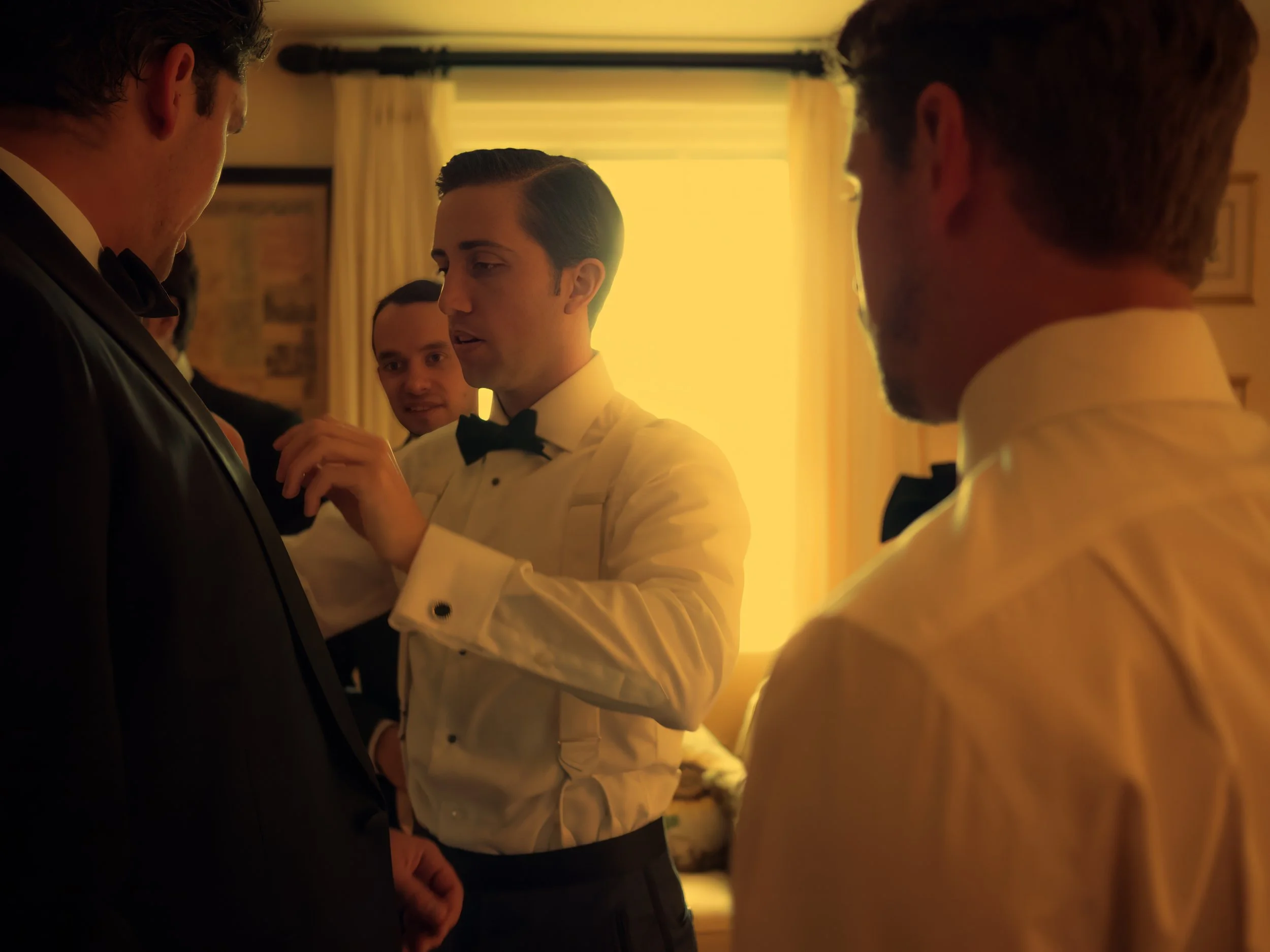 Groom helping a groomsman with his bowtie during wedding preparations in the lower house at Lion Rock Farm.