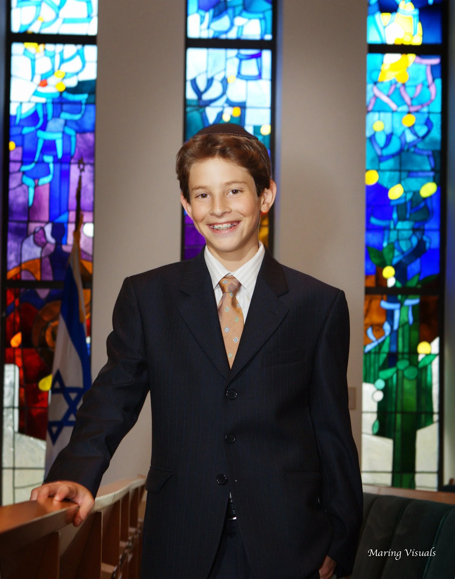 Portrait of a Bar Mitzvah boy standing inside the synagogue during his ceremony day. Caption: