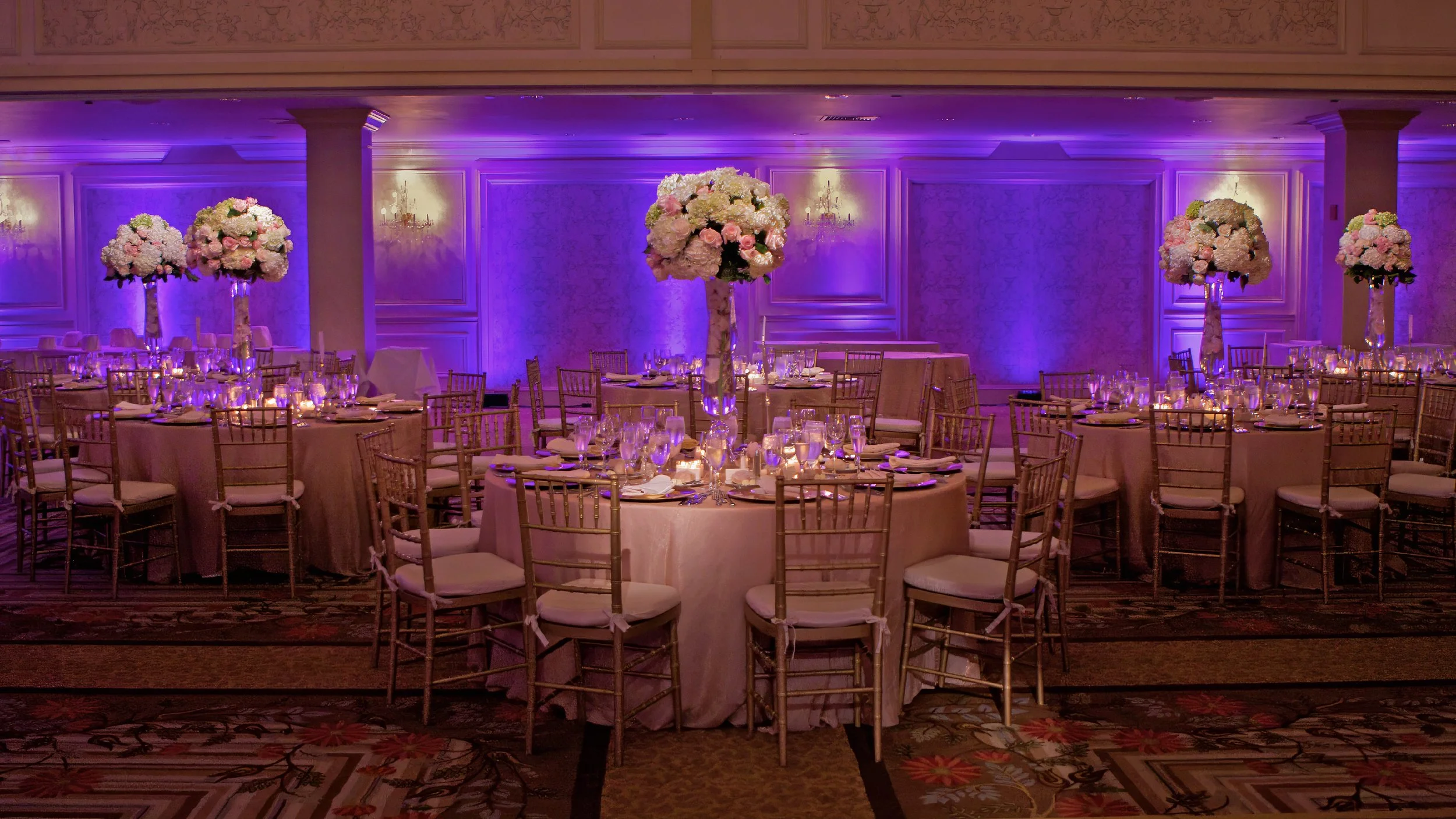 Sweeping view of tables and wedding decor in the Omni Hotel New Haven ballroom. Caption: A sweeping view of the ballroom showcasing the luxurious tables and wedding décor that set the perfect backdrop for celebration.