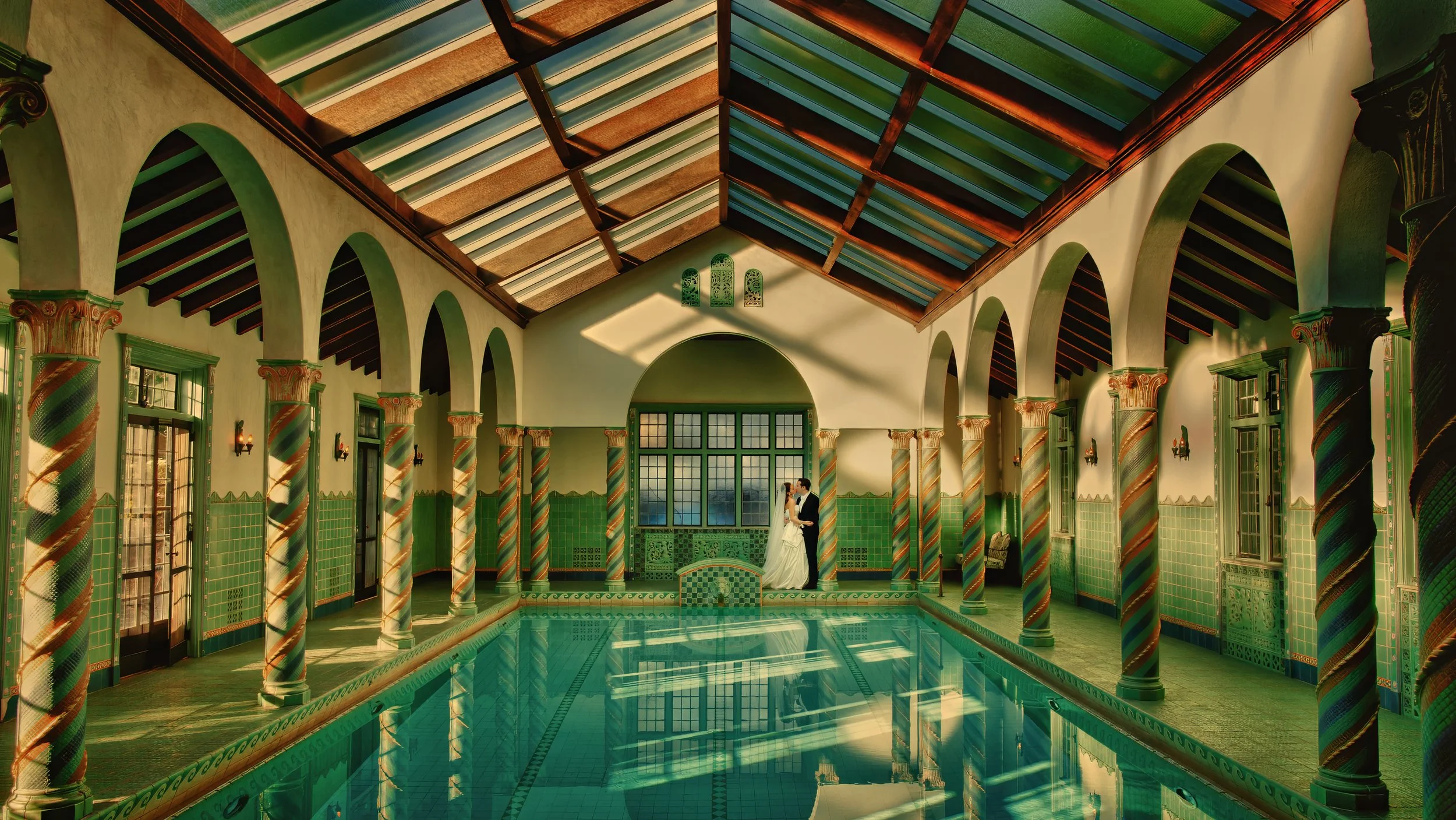 Bride and groom kiss by the indoor pool in a dramatic architectural photograph at Pleasantdale Chateau.