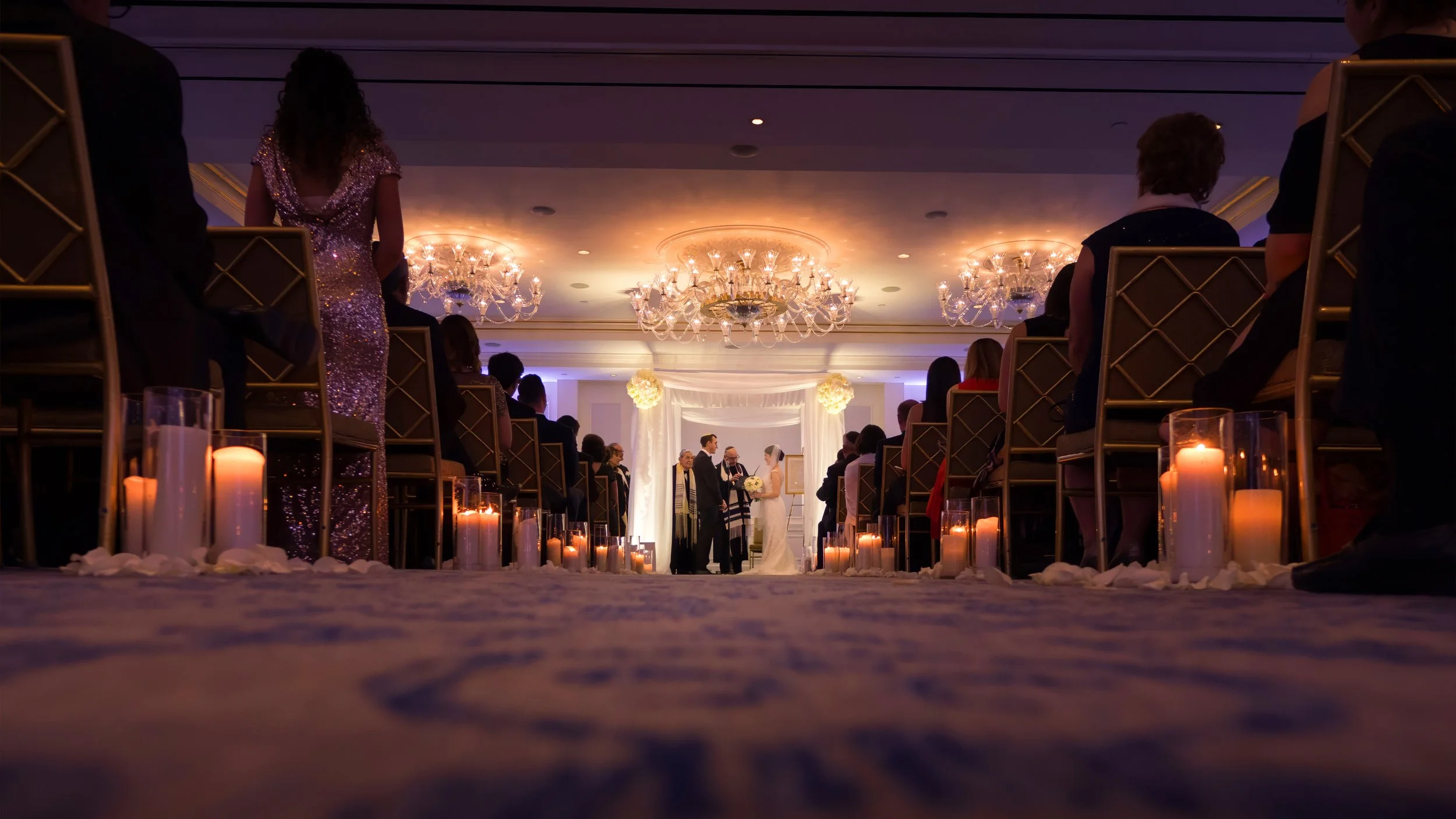 Wide angle photograph of a wedding ceremony taking place in one of the elegant ballrooms at the Lotte New York Palace.