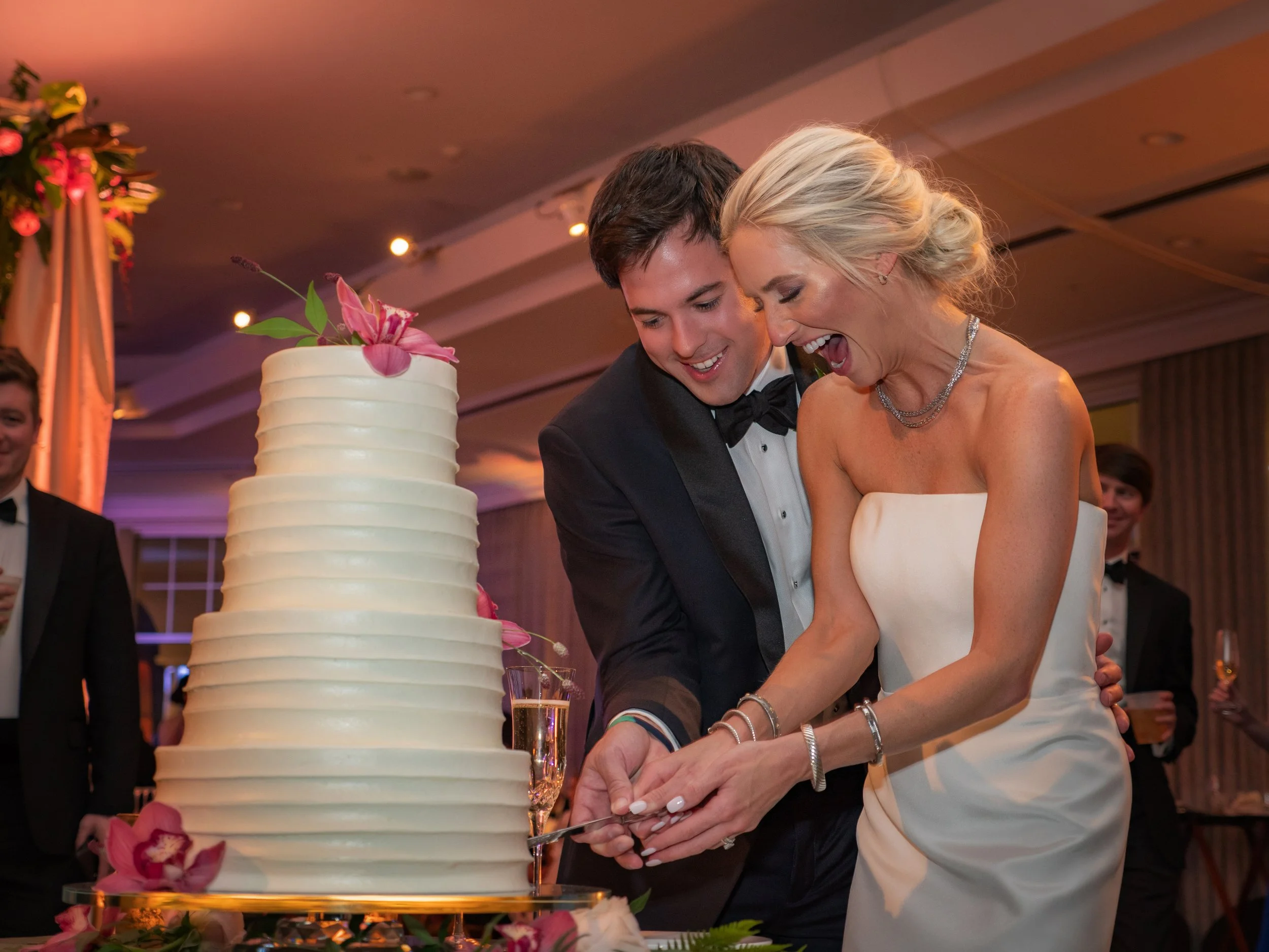 Bride and groom laugh together while cutting their floral wedding cake during an elegant reception.