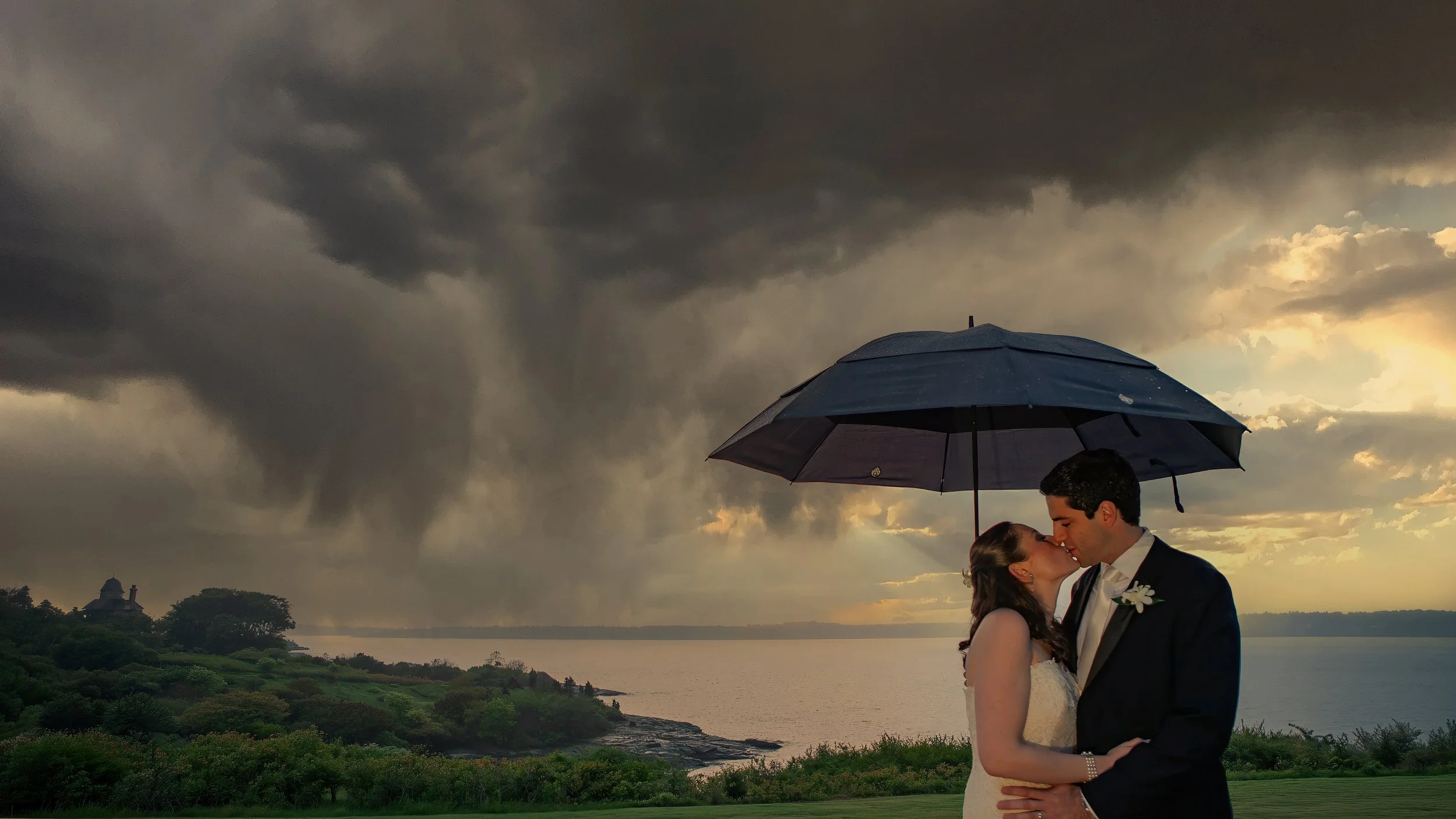 Bride and groom share a kiss beneath rainclouds during a wedding at Ocean Cliff in Newport, Rhode Island.