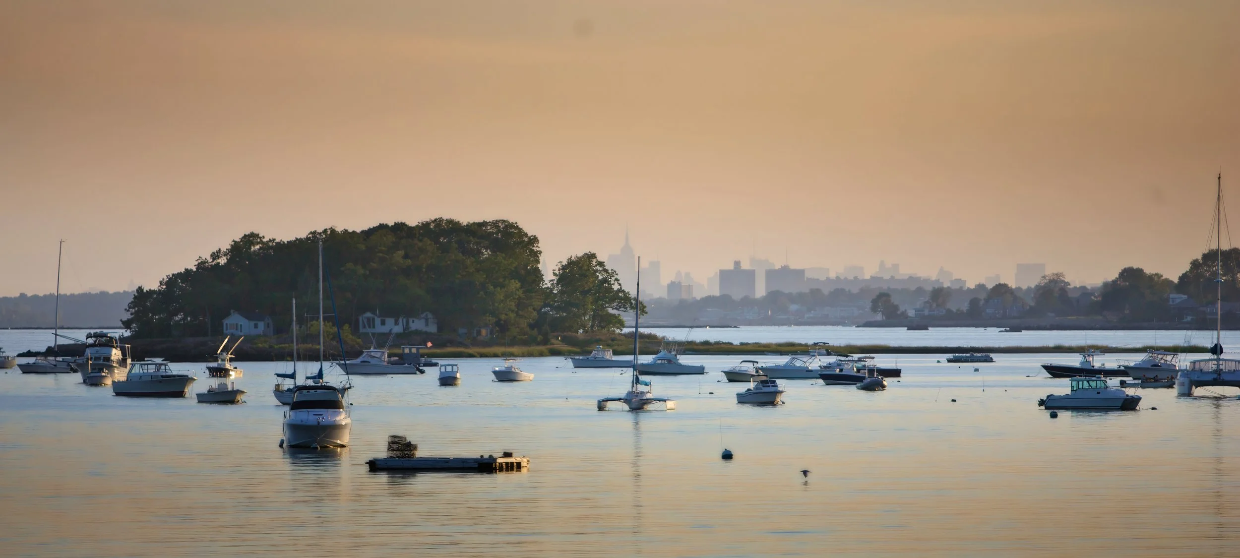 Panoramic view of moored boats on Milton Harbor with Manhattan skyline in the distance at Wainwright House.