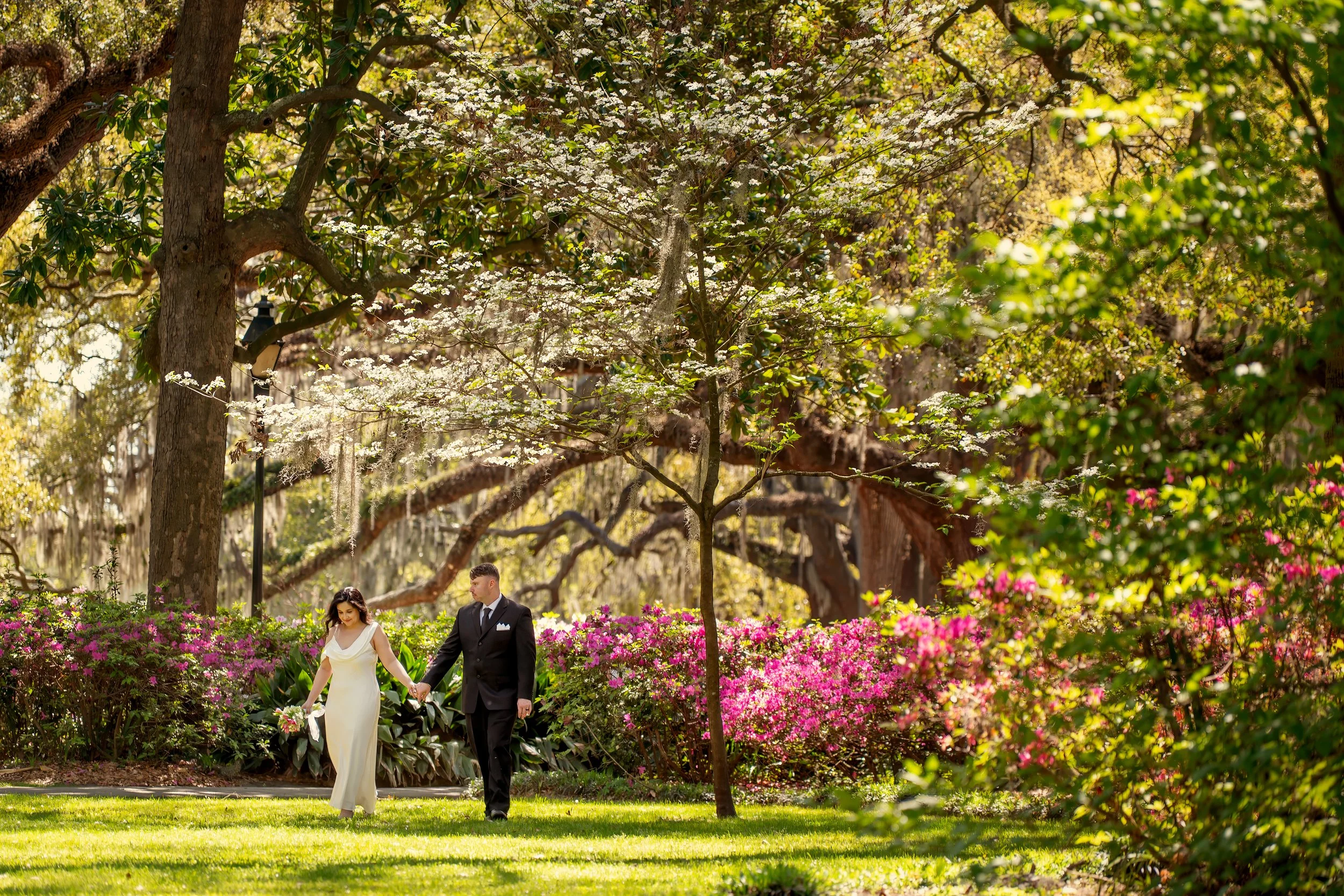 Bride and groom walking through blooming azaleas during a spring wedding in Forsyth Park Savannah.