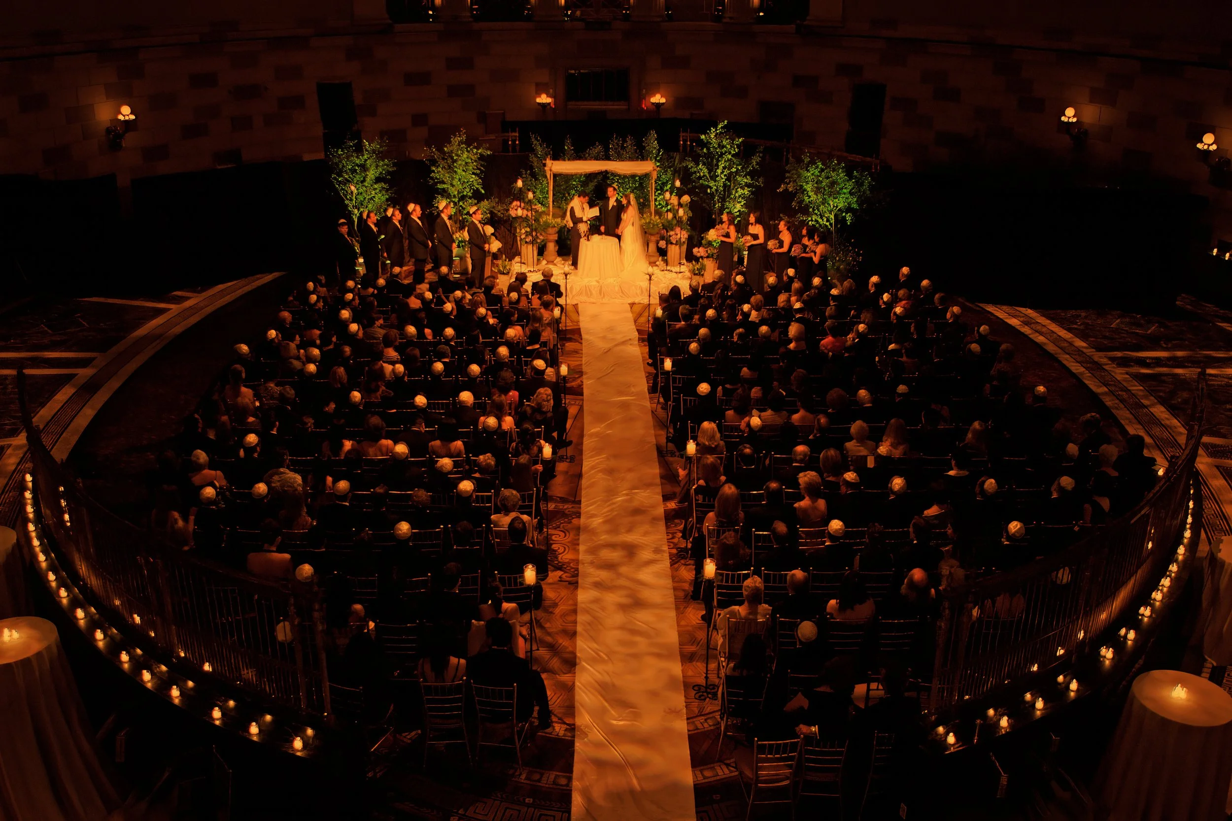 Bride and groom exchange vows during a wedding ceremony at Gotham Hall beneath warm amber lighting in New York City.