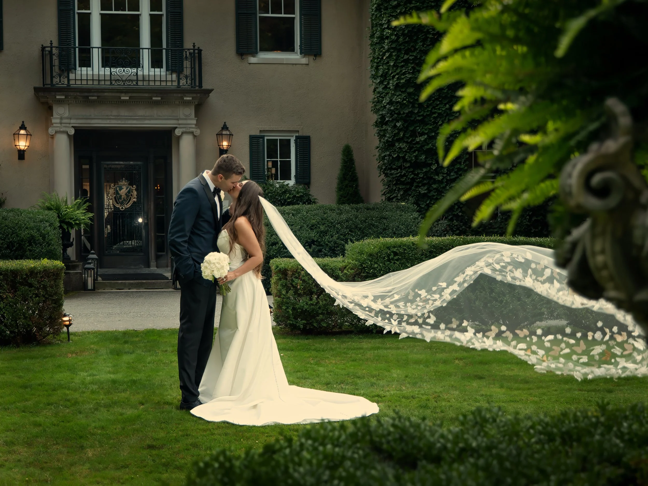 Bride and groom kissing with veil blowing in wind at Lord Thompson Manor wedding Connecticut