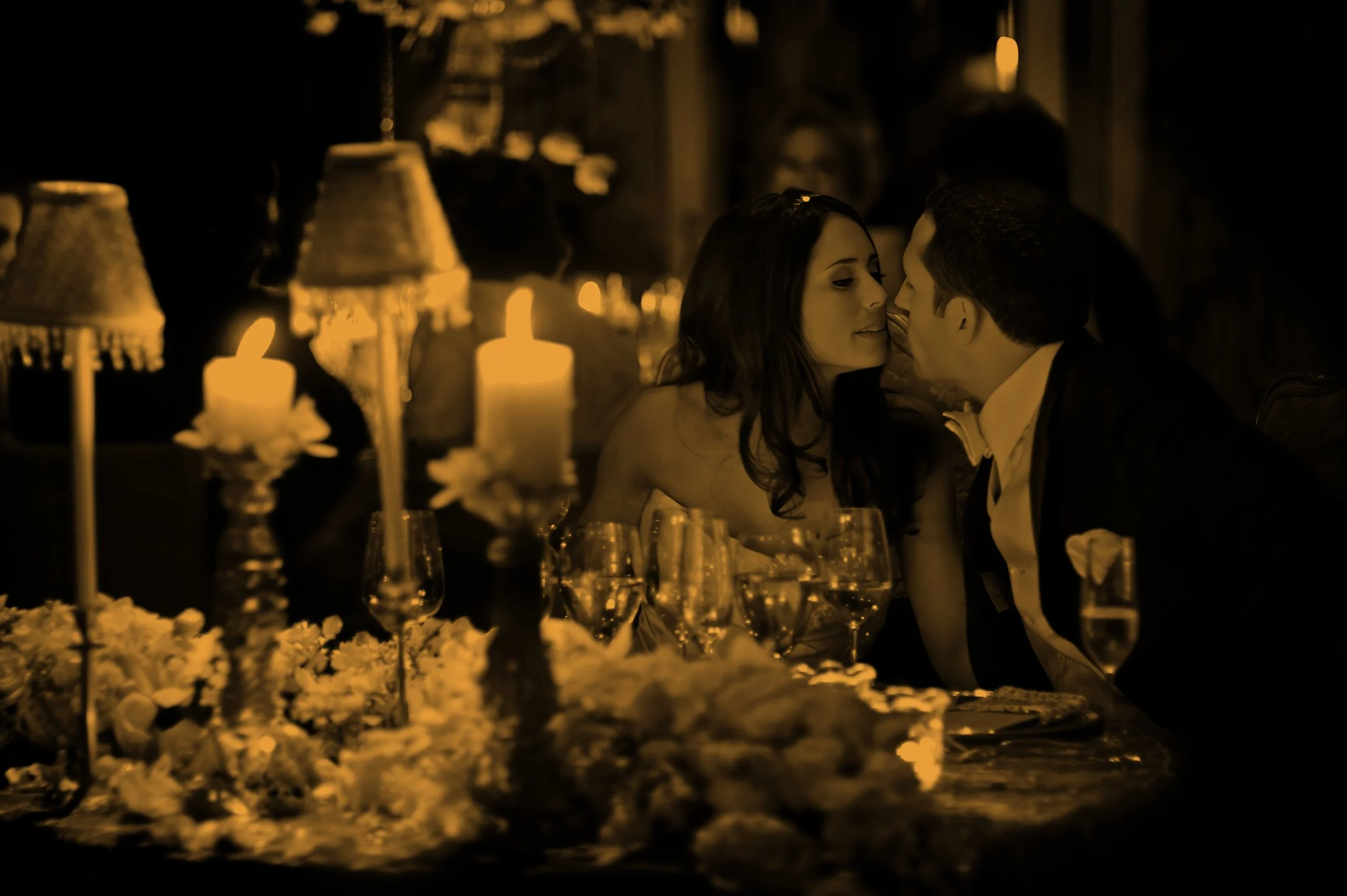 Bride and groom share an intimate kiss at their candlelit wedding reception table.