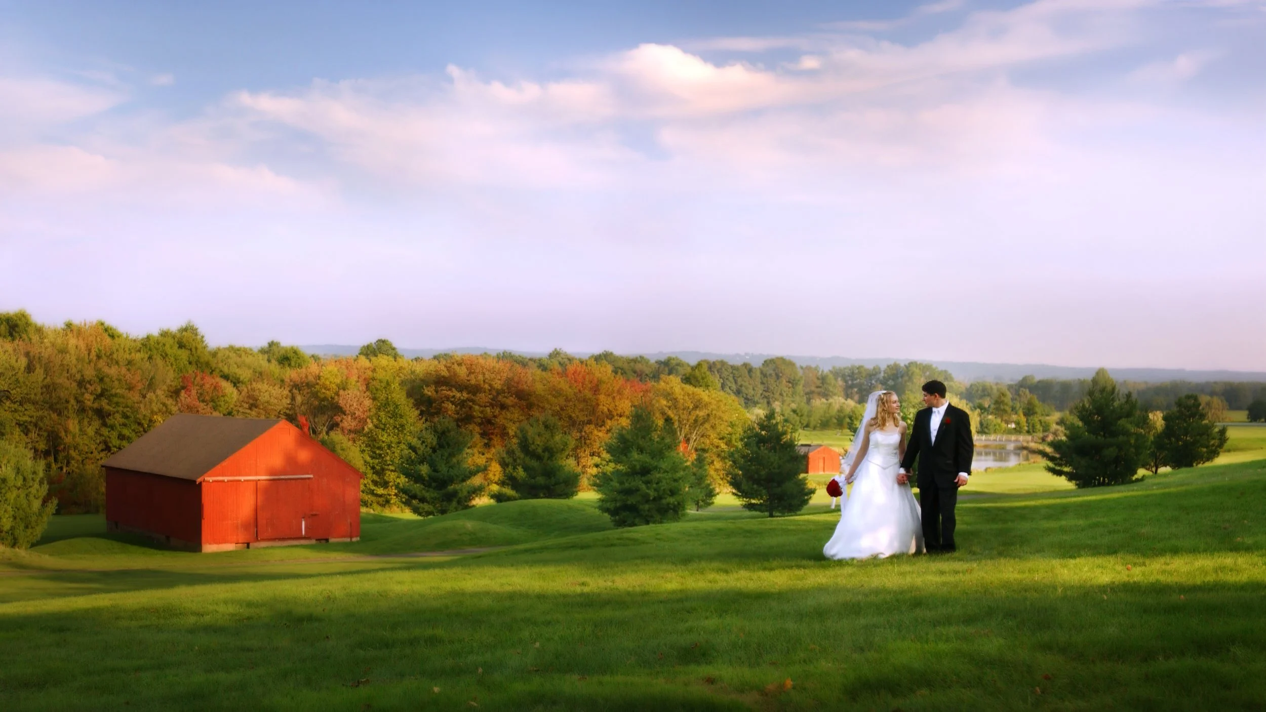 Bride and groom walking hand in hand at The Lyman Homestead in Middlefield, Connecticut surrounded by early fall foliage.