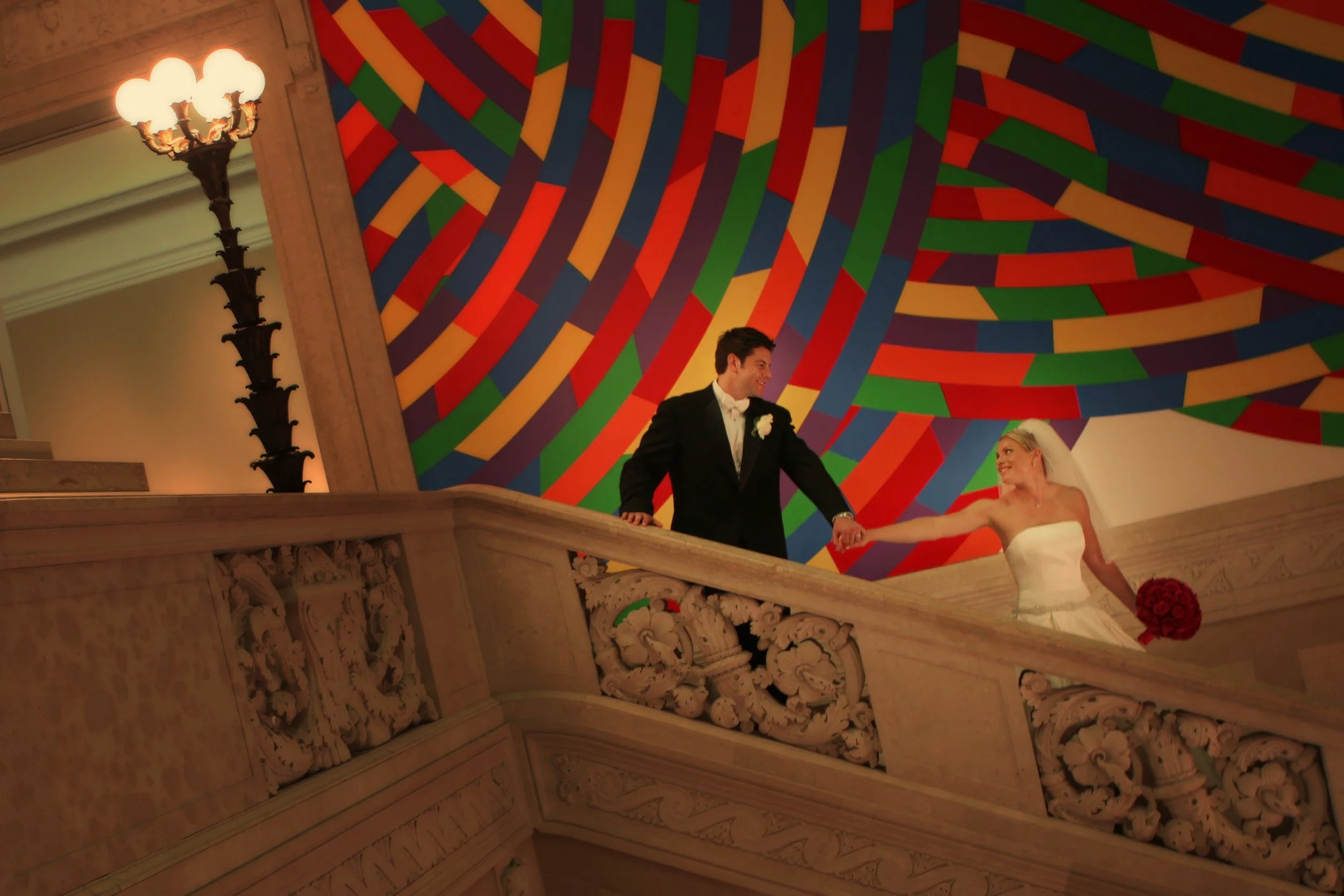 Bride leads groom down the staircase in the art-filled halls of Wadsworth Atheneum.