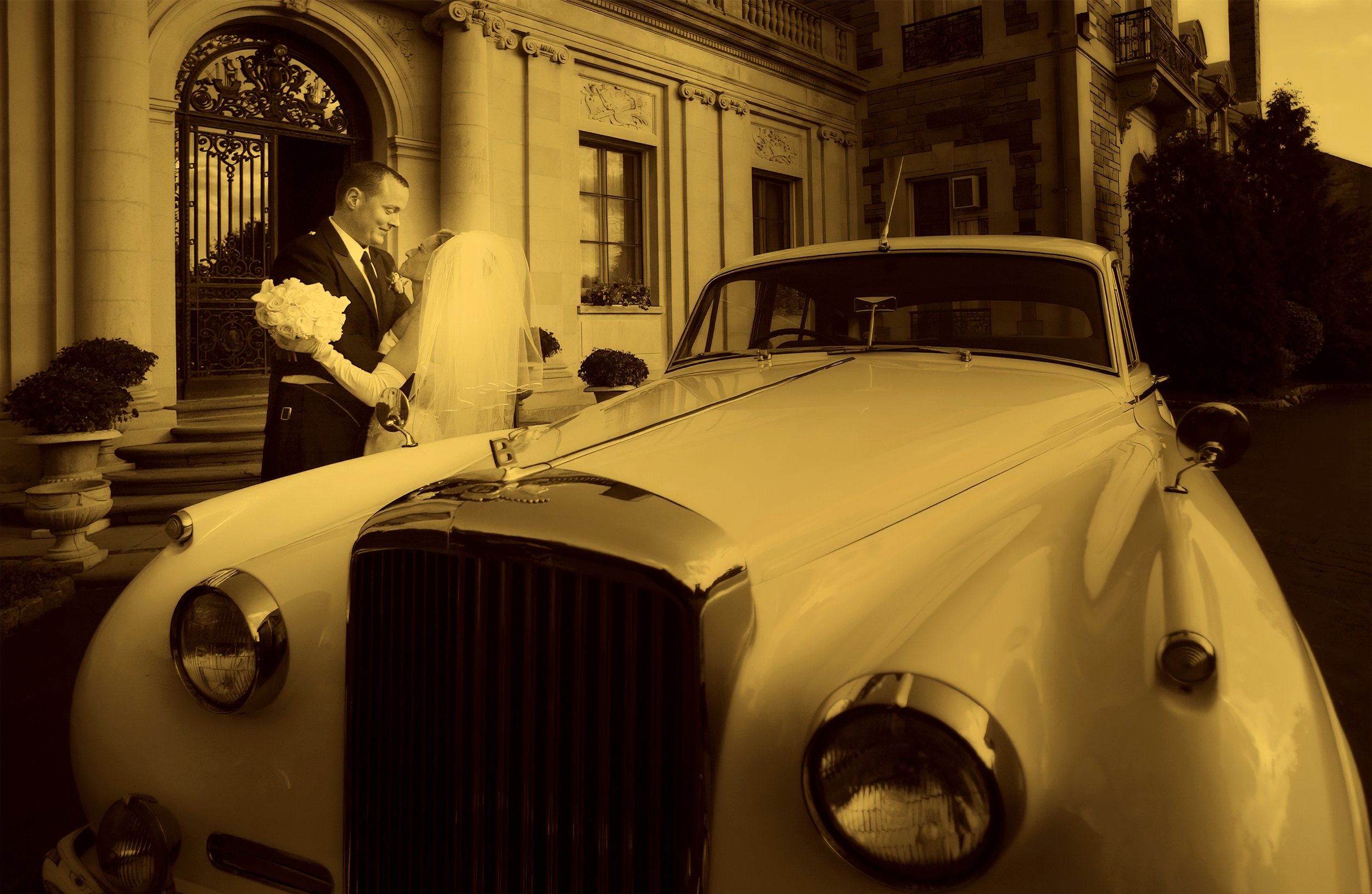 Bride and groom posing with a vintage limousine beneath the grand entrance of Aldrich Mansion.